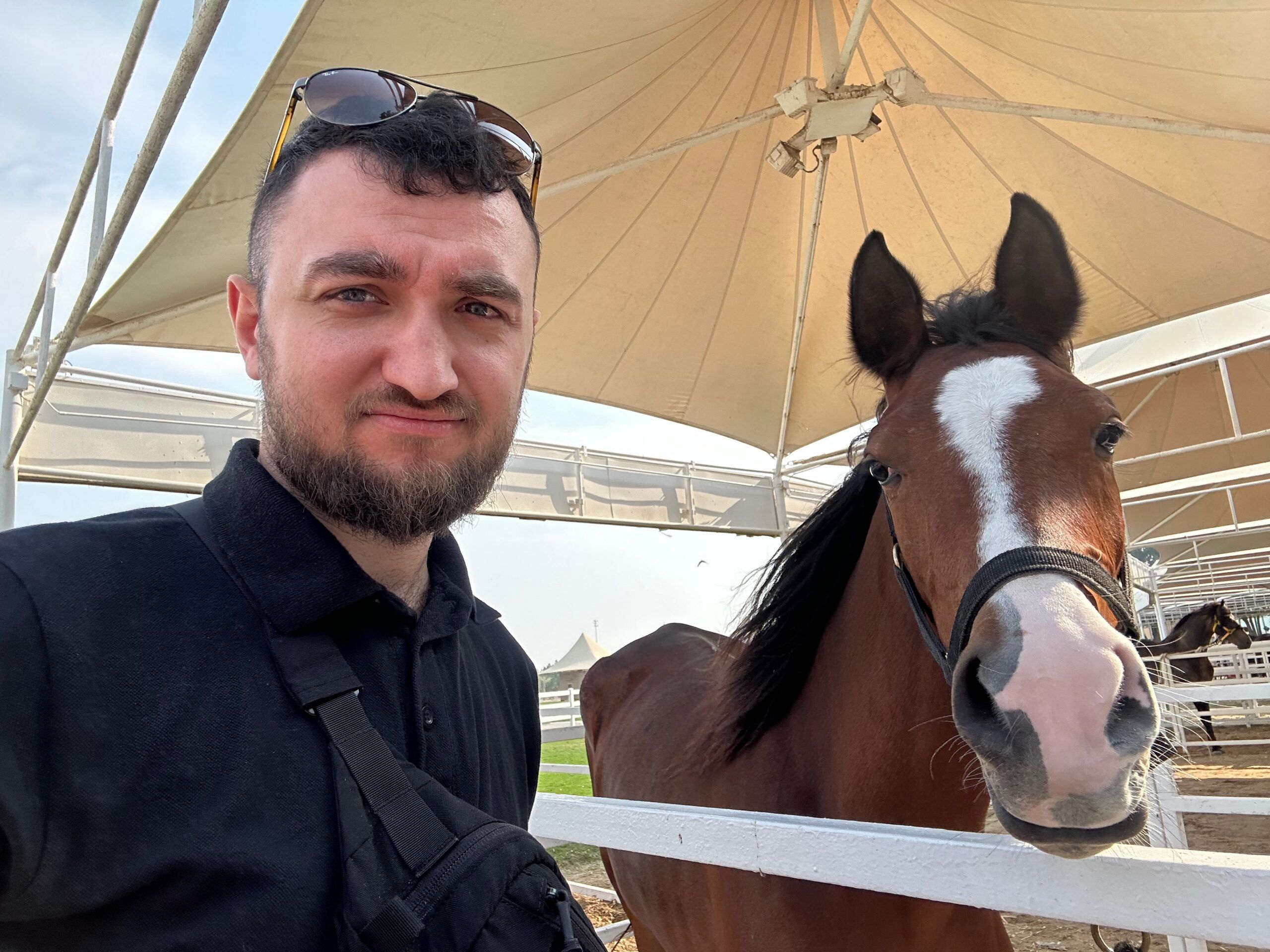 Mężczyzna robi selfie obok konia pod zadaszeniem w bahrainie.