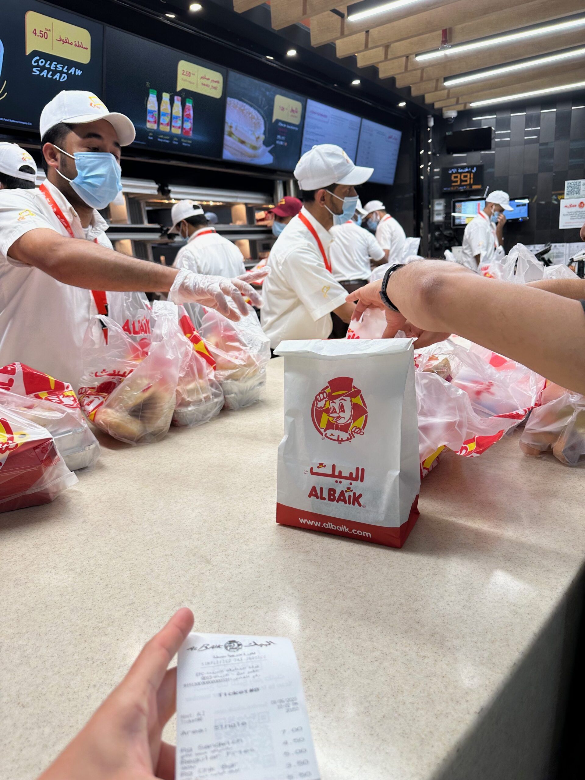 Obsługa w restauracji albaik w arabii saudyjskiej wydaje zamówienia przy ladzie.