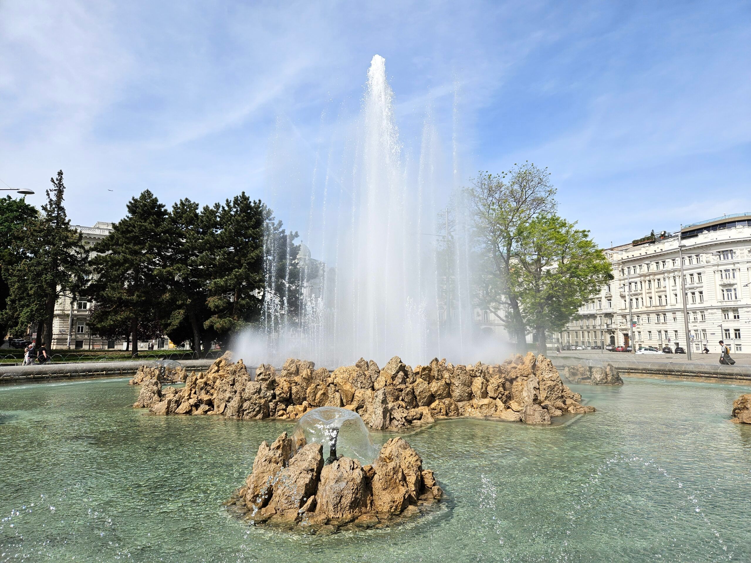 Fontanna na schwarzenbergplatz w wiedniu z wysokim strumieniem wody i otaczającymi ją budynkami.