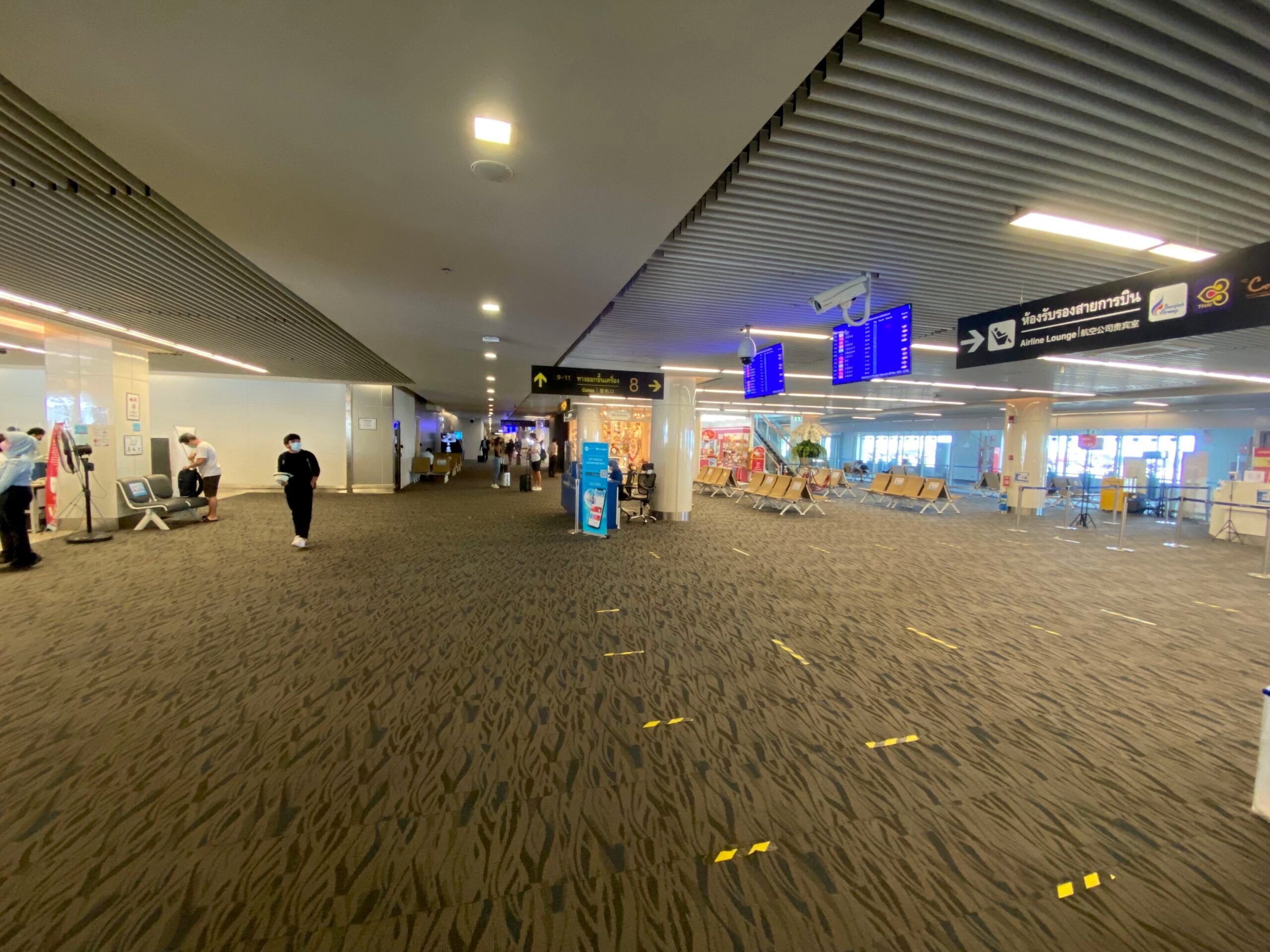 Terminal lotniska w tajlandii z tablicami odlotów i kilkoma pasażerami.