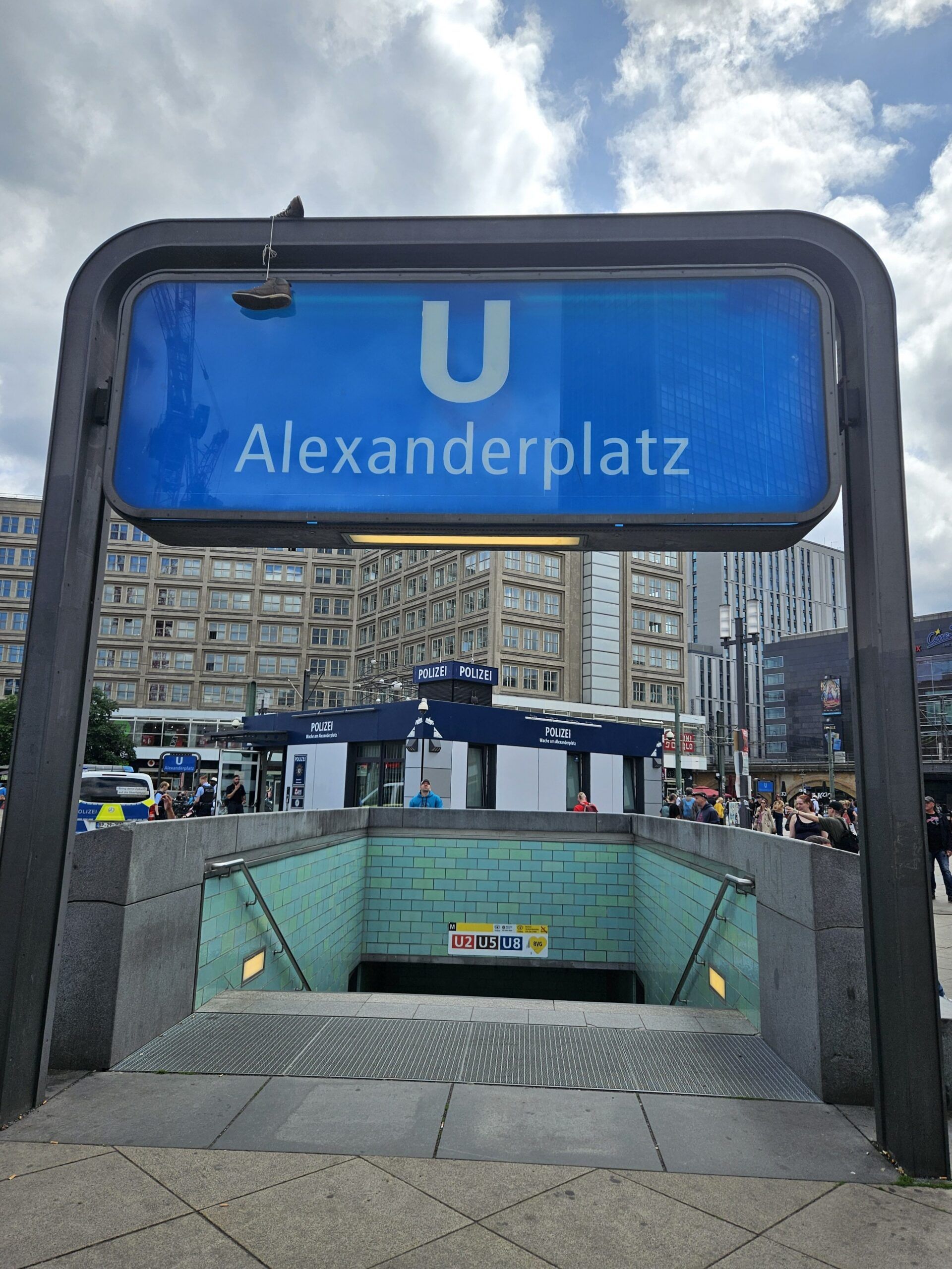Wejście do stacji u alexanderplatz w berlinie, z niebieskim znakiem nad schodami.