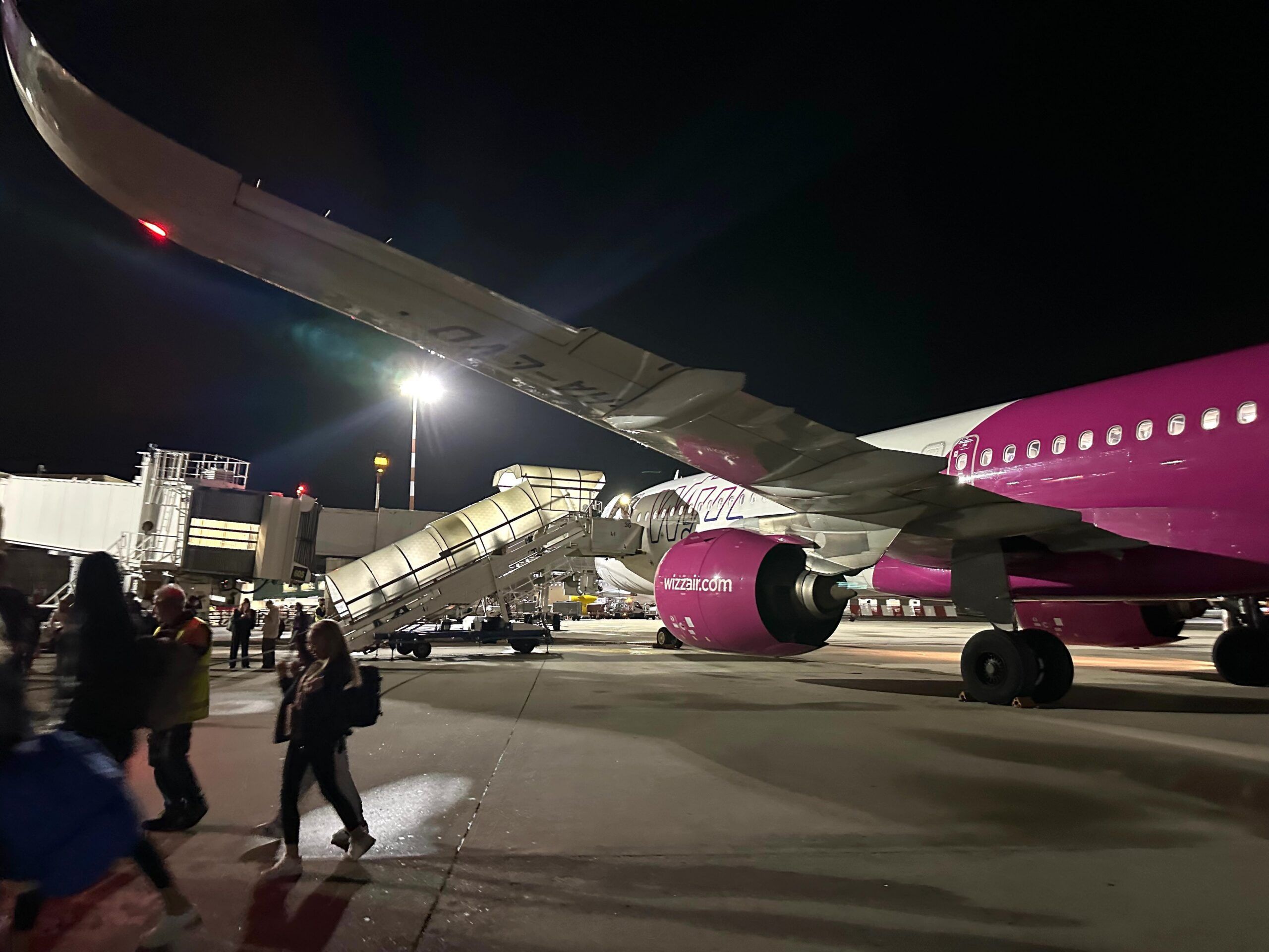 Samolot wizz air na płycie lotniska w mediolanie nocą, z pasażerami wysiadającymi po schodach.