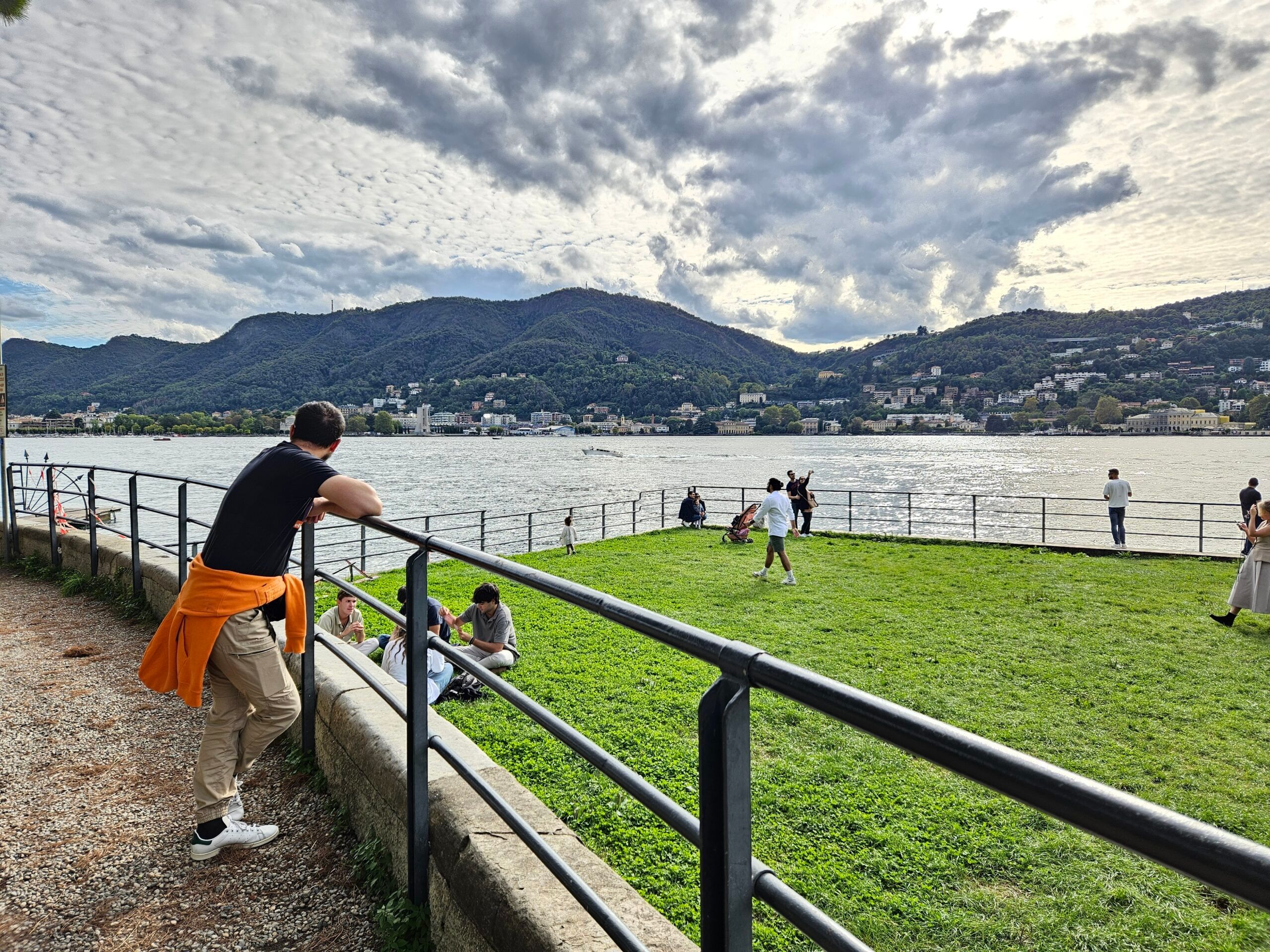 Como nad jeziorem, z ludźmi odpoczywającymi na promenadzie i górami w tle