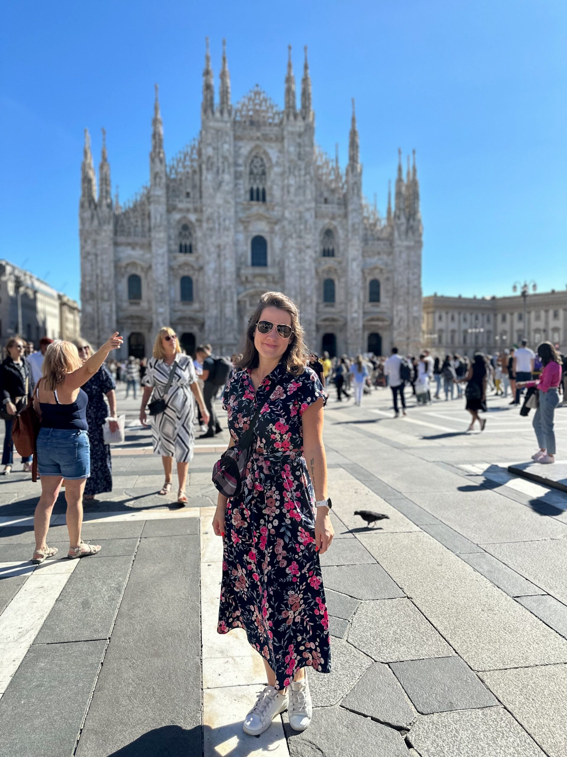 Kobieta w kwiecistej sukience stoi przed katedrą duomo w mediolanie.