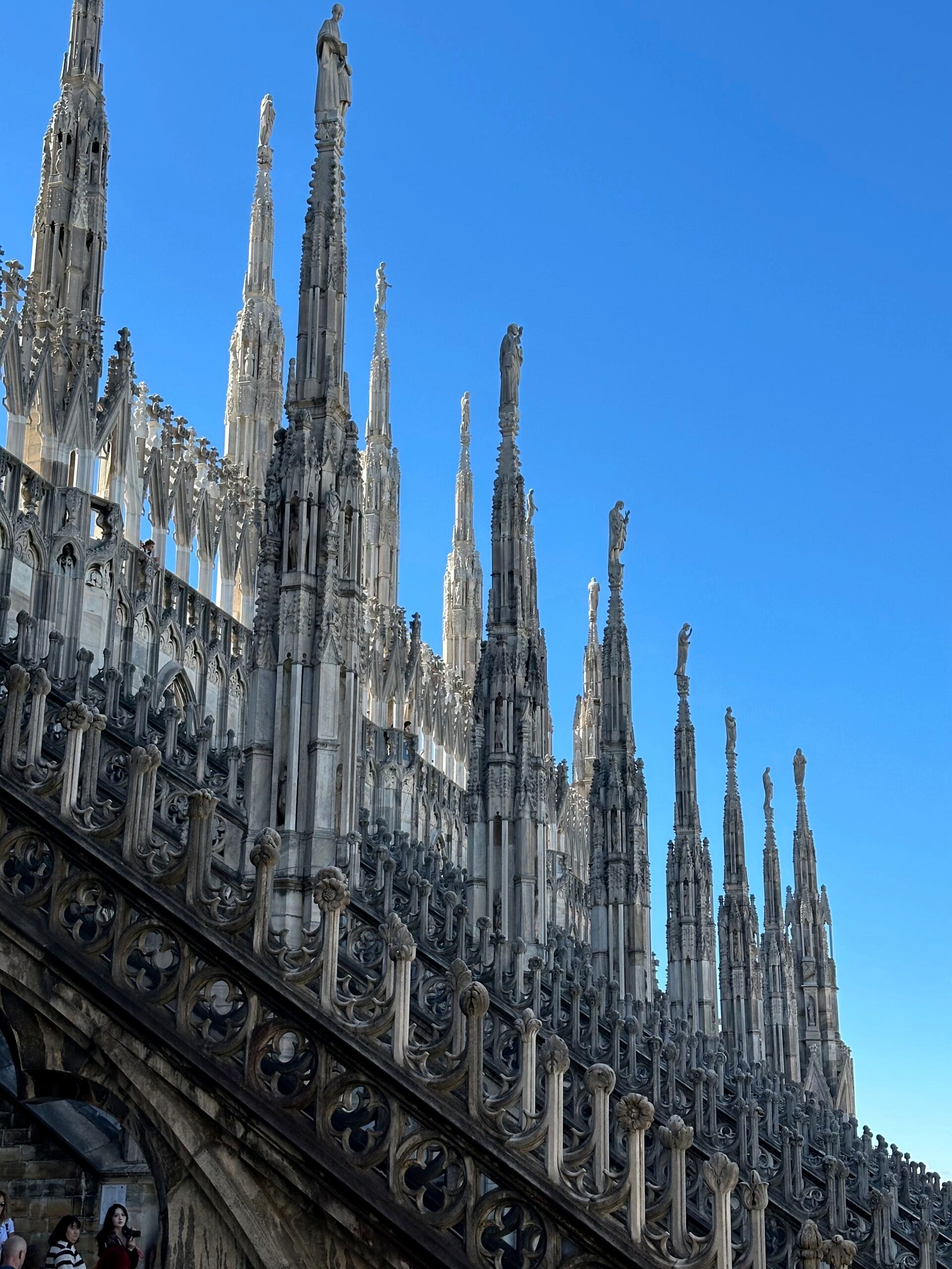Katedra duomo w mediolanie z gotyckimi wieżyczkami i figurami na tle błękitnego nieba