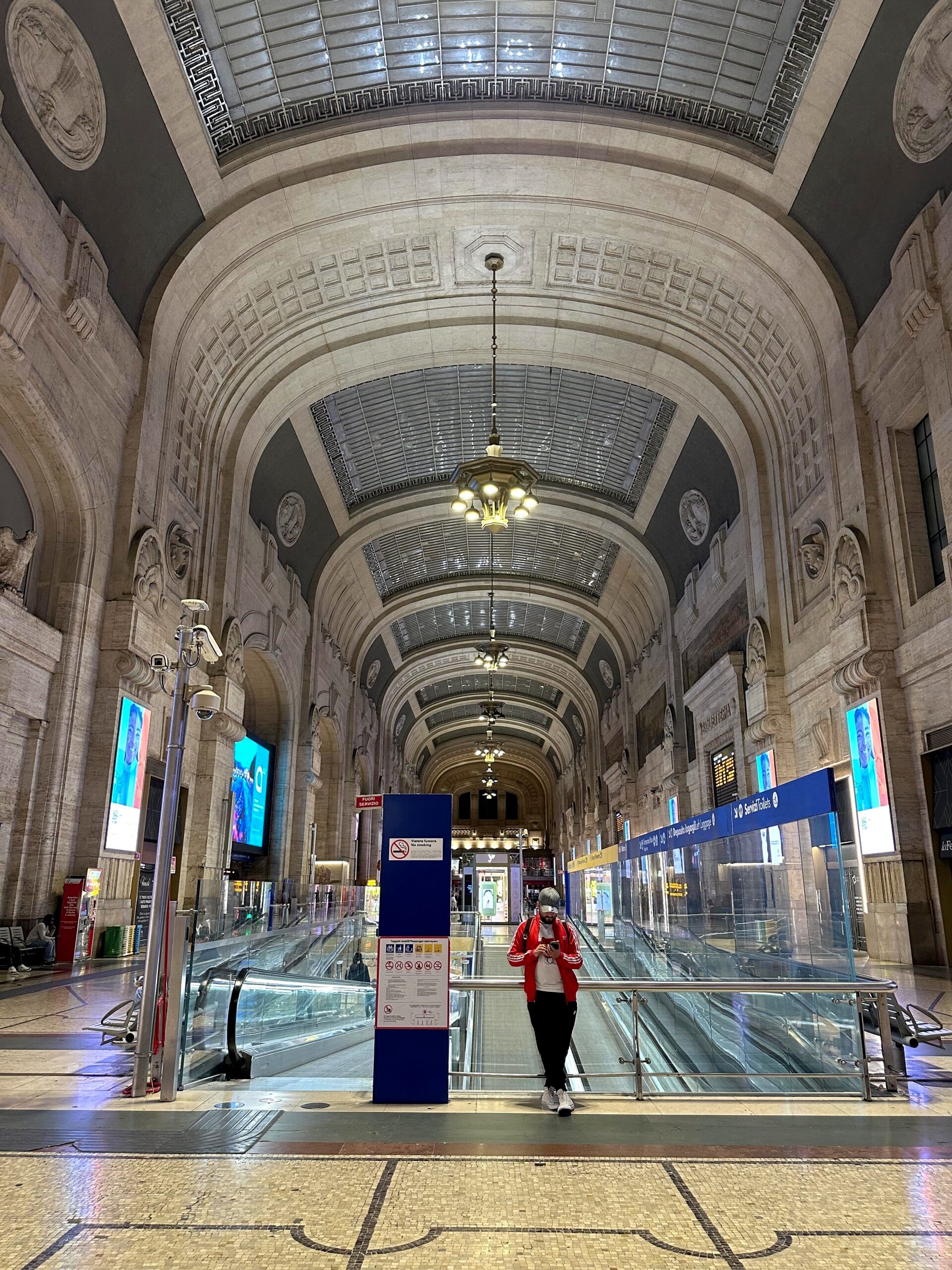 Wnętrze dworca milano centrale z wysokimi arkadami i ruchomymi schodami w centrum.