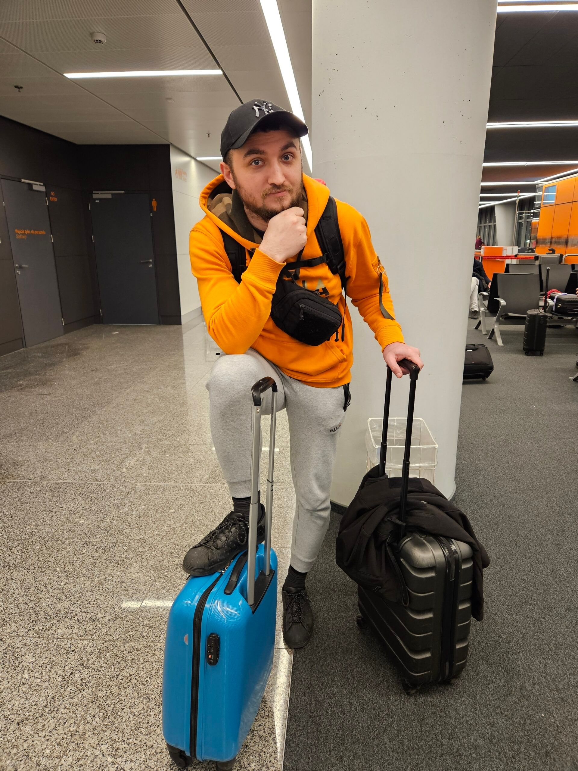 Filip on airport: man with lost luggage standing with blue suitcase and black backpack in an airport hallway