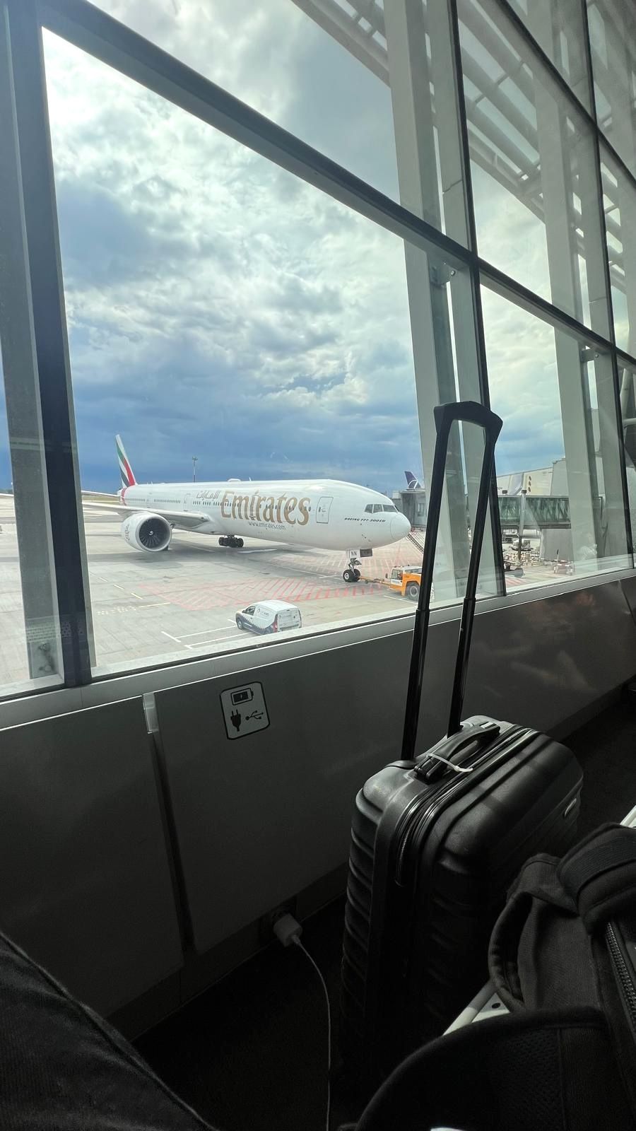View of an emirates airplane at the airport gate through a window with luggage in the foreground