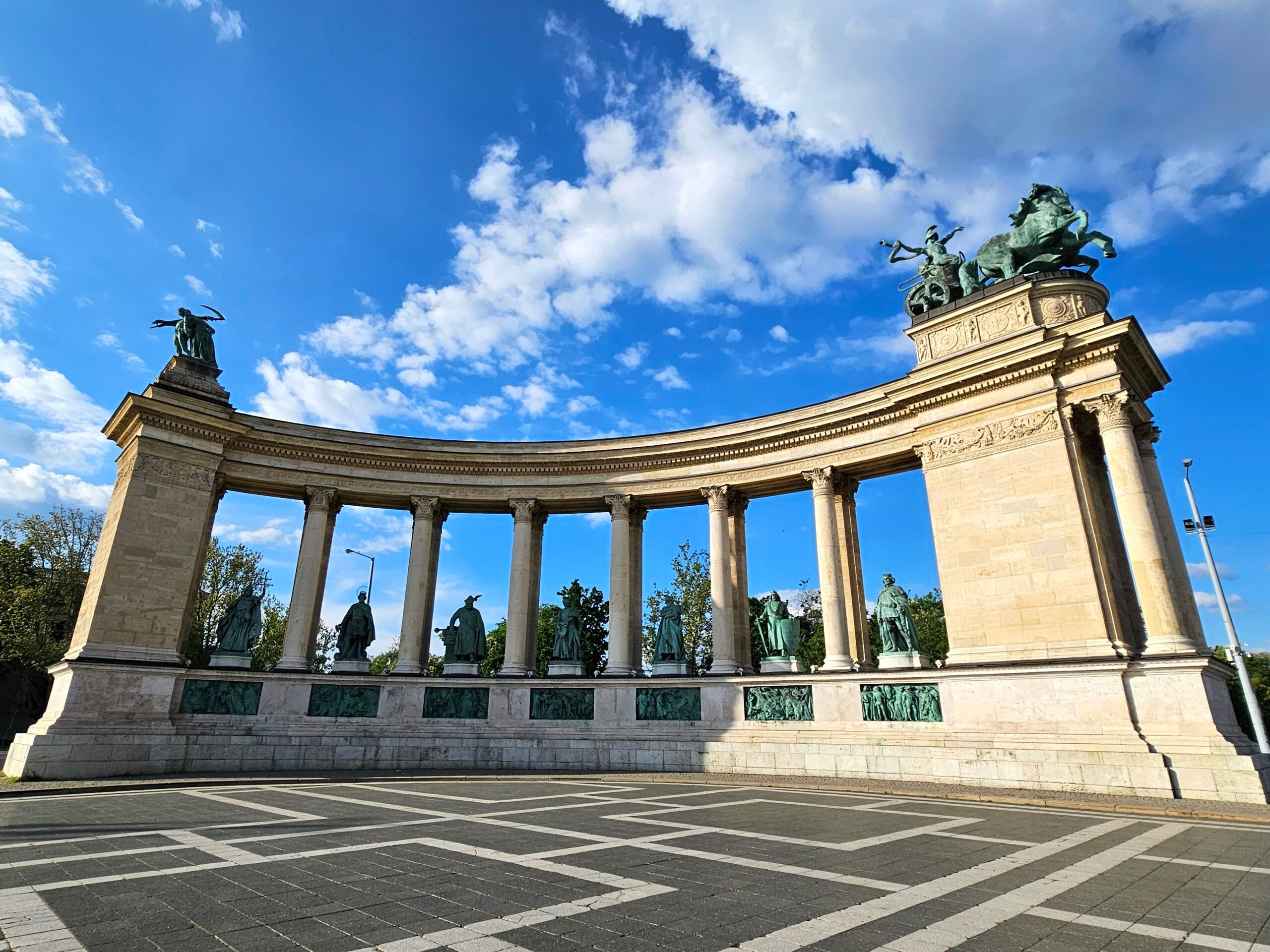 Plac bohaterów w budapeszcie z półkolistą kolumnadą i posągami na tle błękitnego nieba