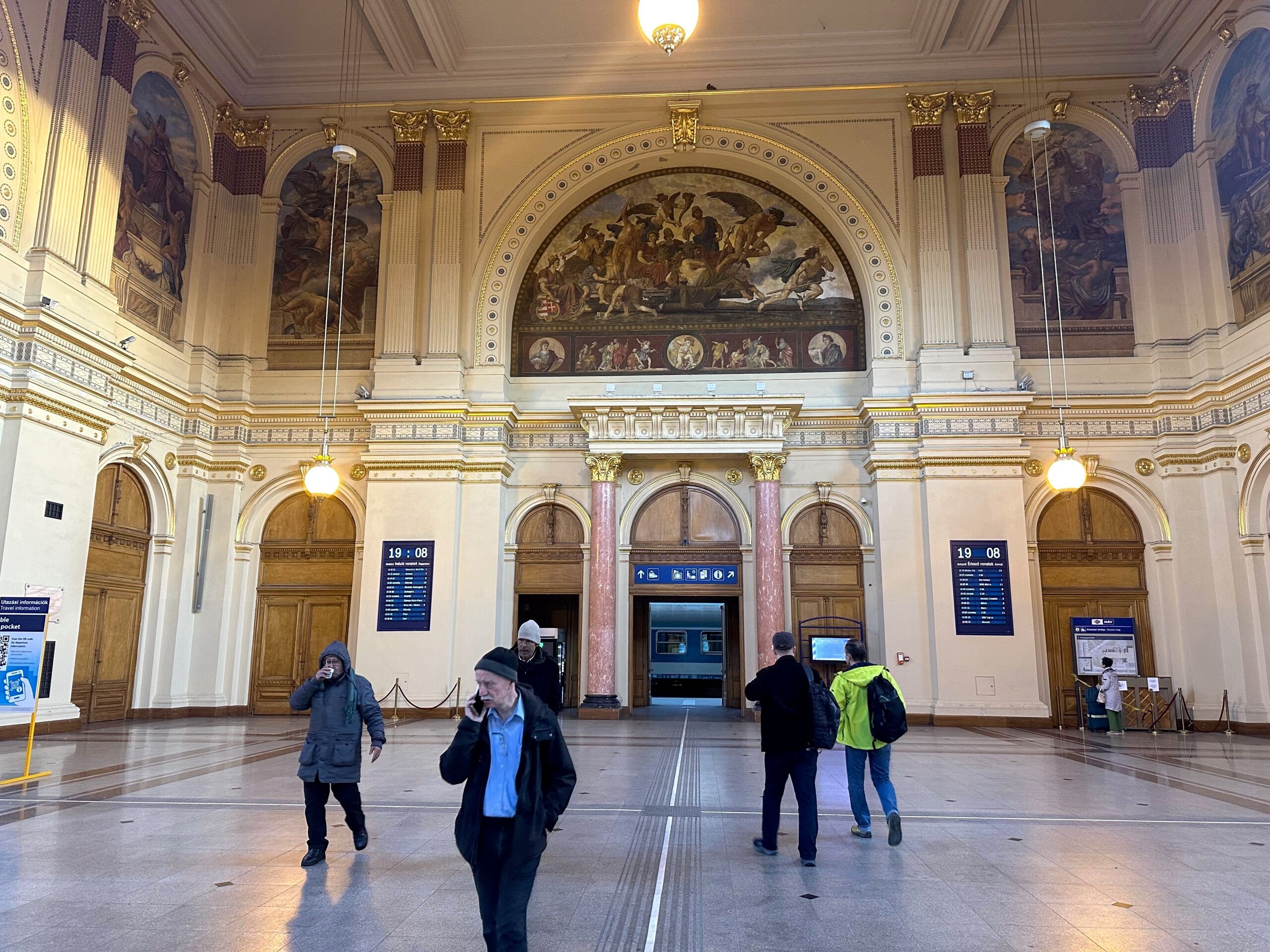 Dworzec główny w budapeszcie z ozdobną halą i kilkoma pasażerami.
