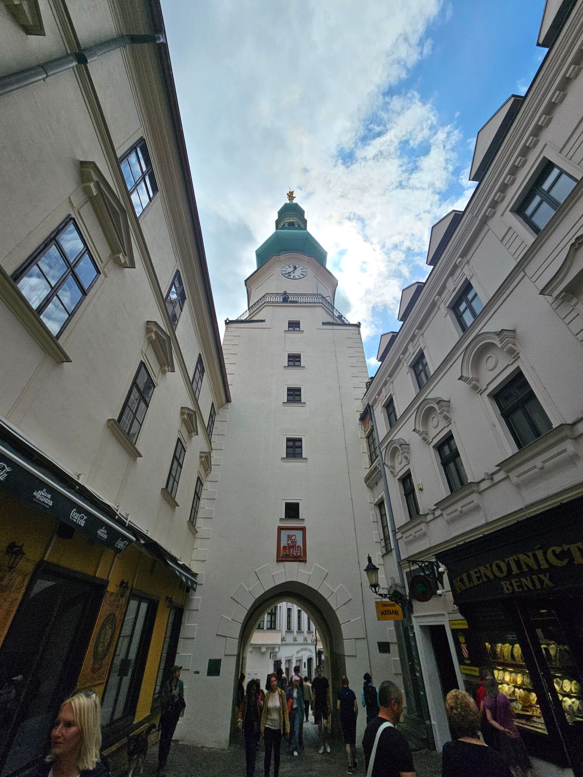 Brama michała w bratysławie, widok z wąskiej uliczki z przechodniami.