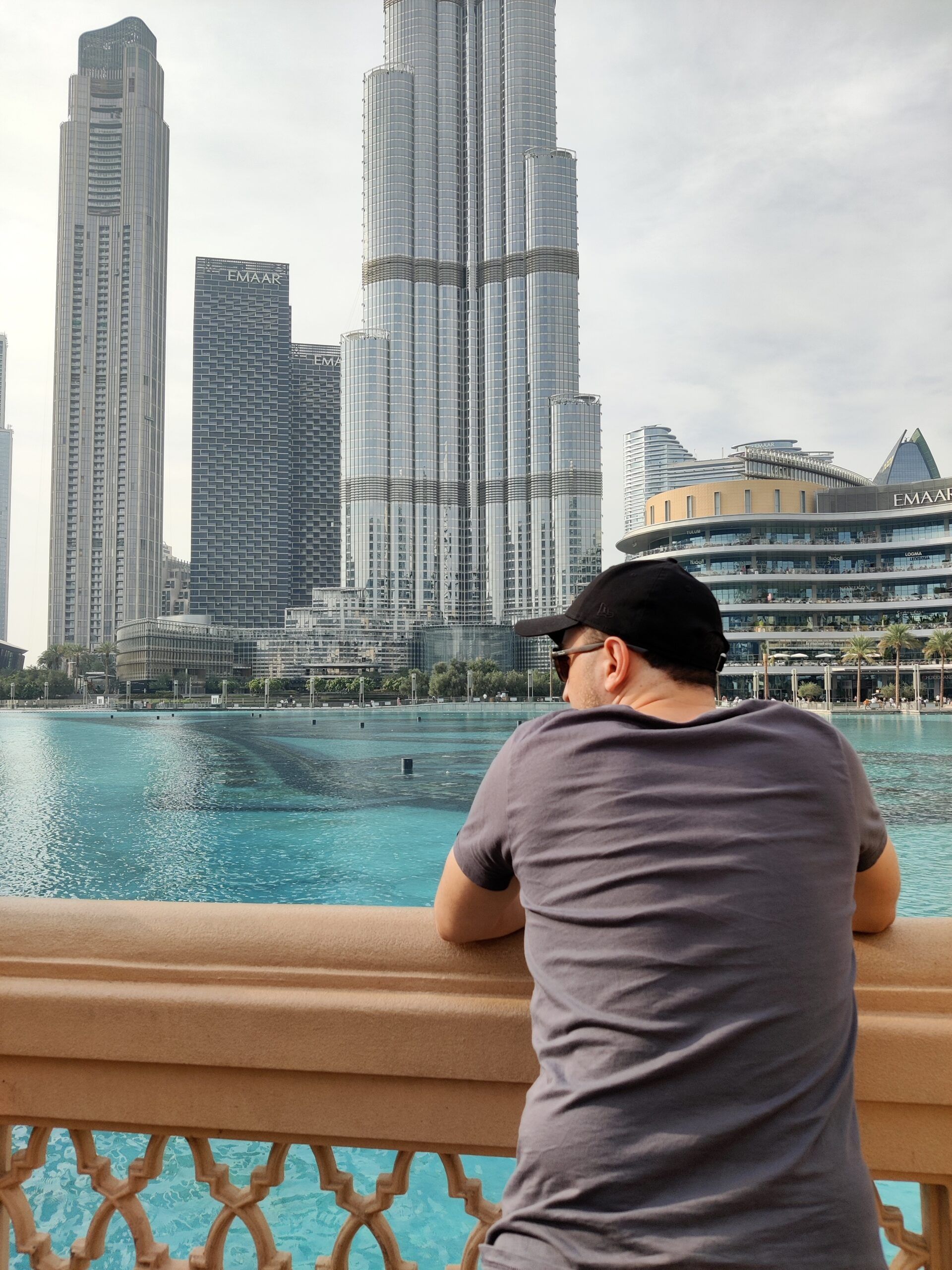 Mężczyzna opiera się o barierkę przy dubai fountain, patrząc na wieżowce w dubaju.