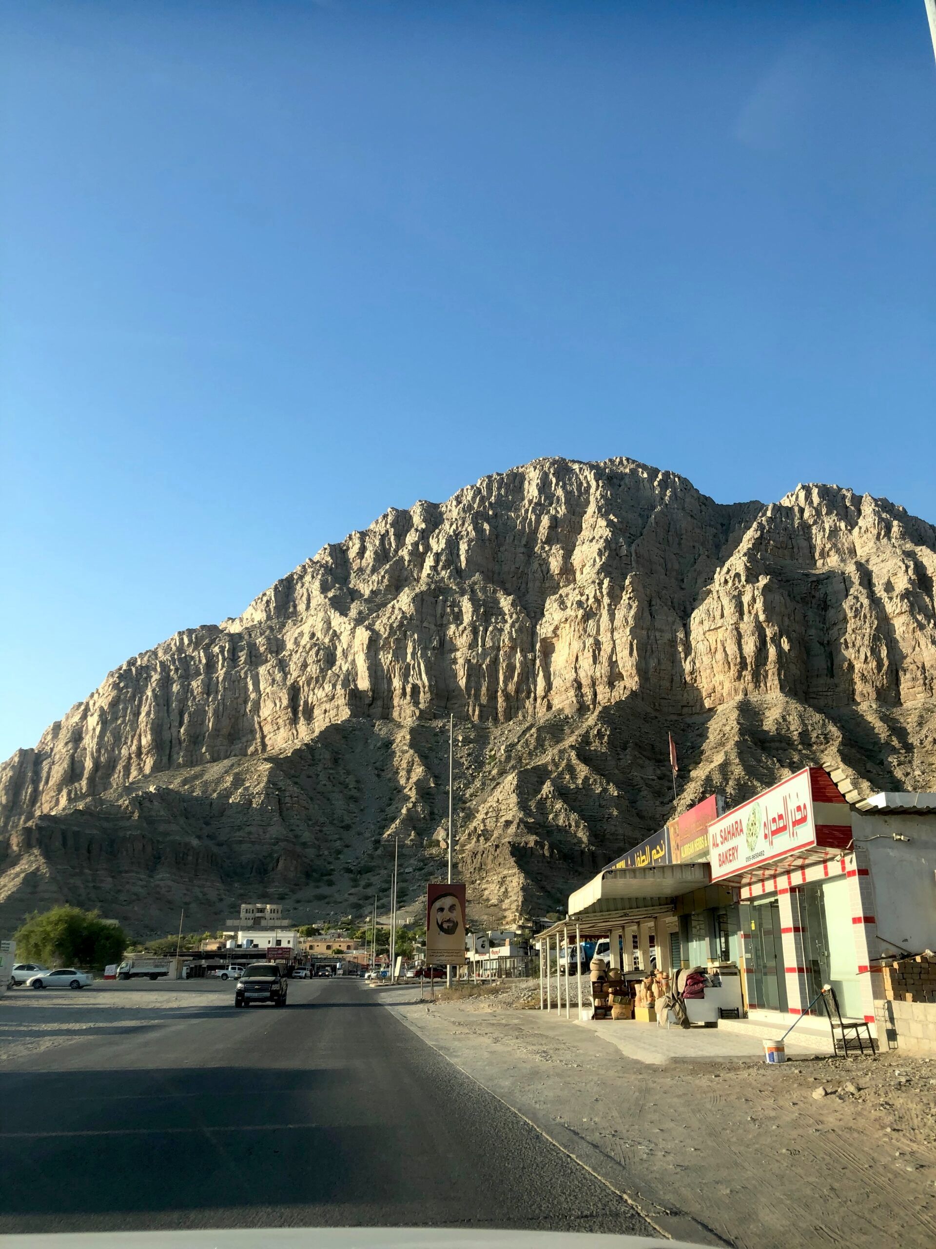 Droga u podnóża skalistej góry w ras al khaimah w zea, z lokalnymi sklepami po prawej.