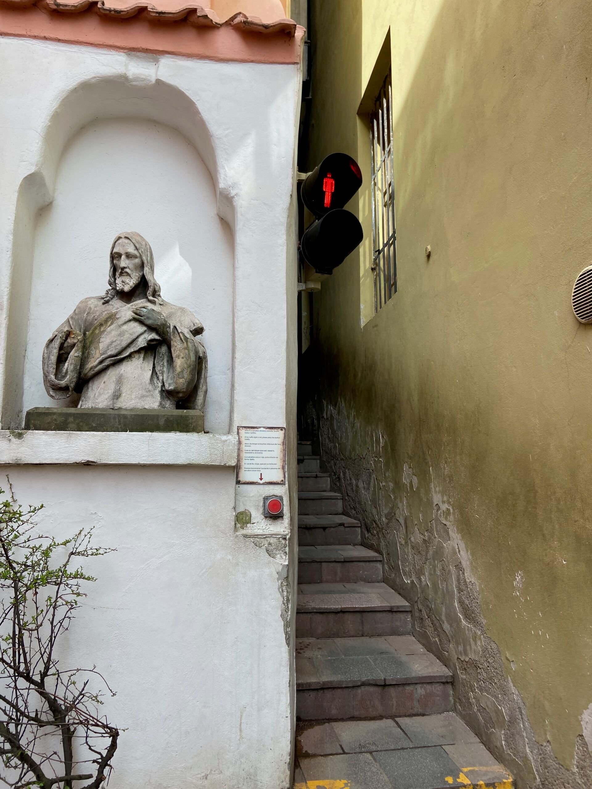 Praga: wąska uliczka ze schodami, rzeźbą świętego i czerwonym światłem na sygnalizacji.