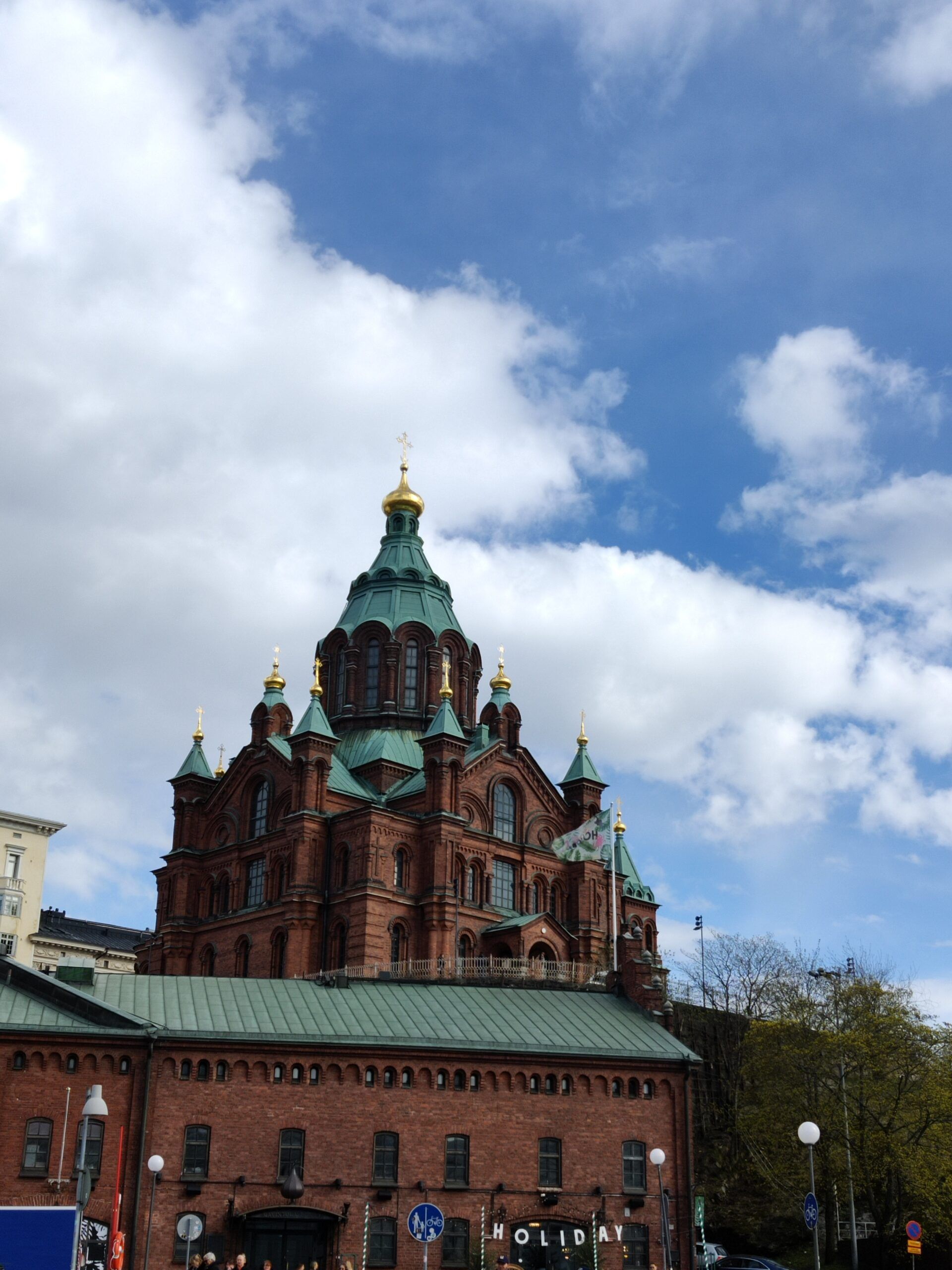 Sobór uspieński w helsinkach z czerwonymi cegłami i zielonymi kopułami pod częściowo chmurnym niebem