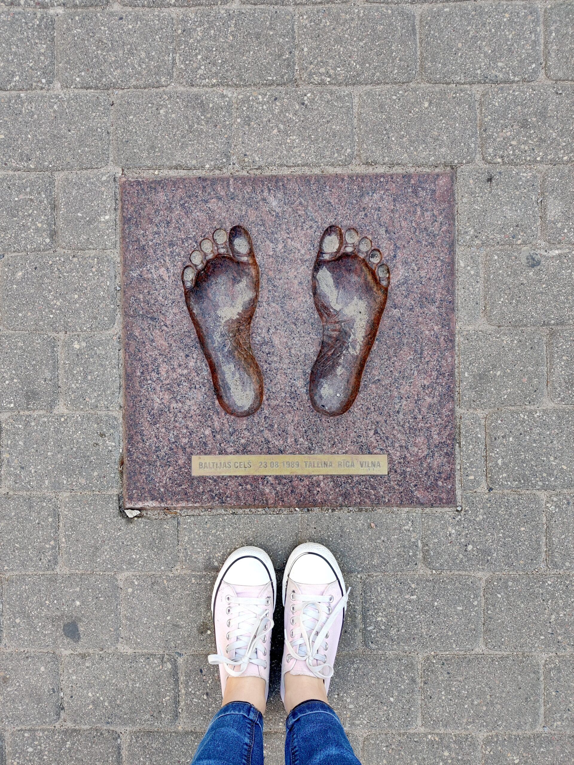 Ślady stóp przy pomniku wolności w rydze, obok stoją białe trampki.