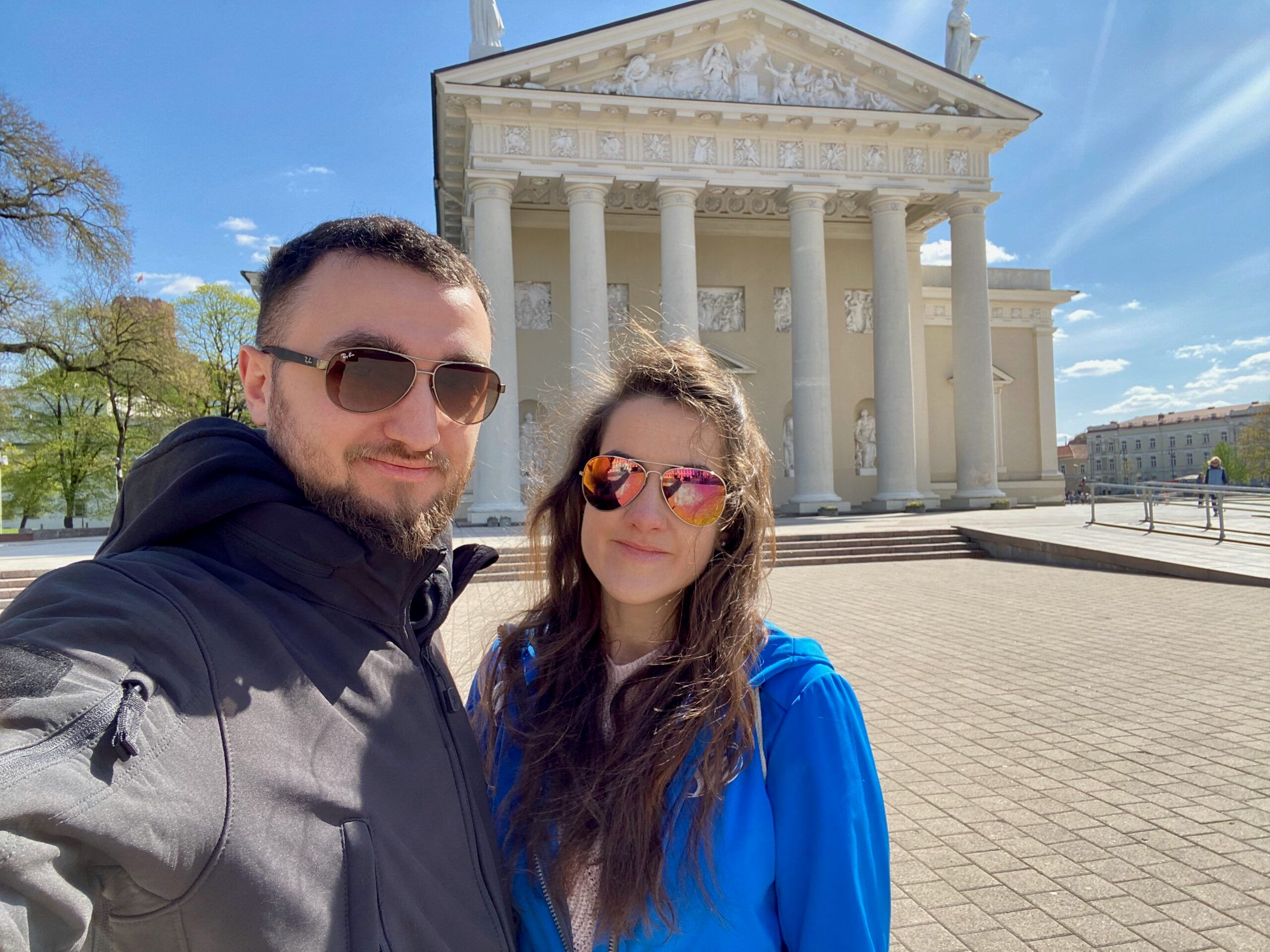 Selfie dwojga osób przed katedrą w wilnie, z białą kolumnadą w tle