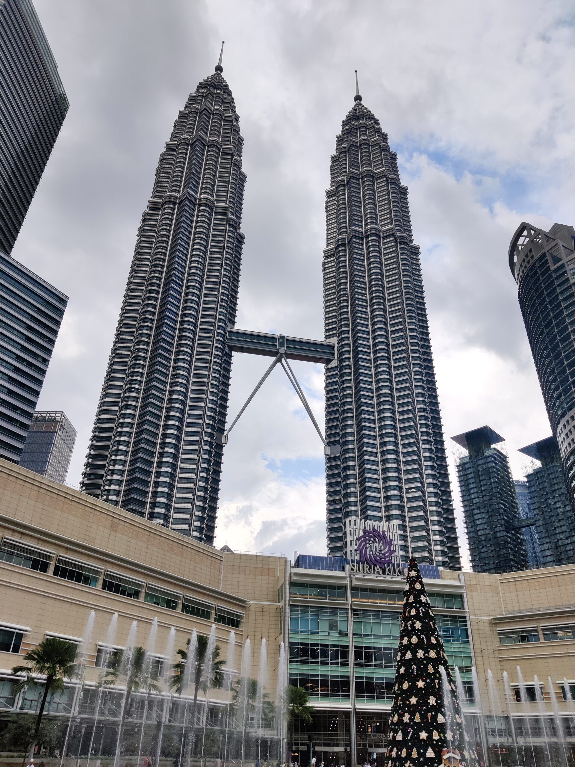 Bliźniacze wieże petronas w kuala lumpur nad centrum handlowym suria klcc, z fontannami i choinką na placu