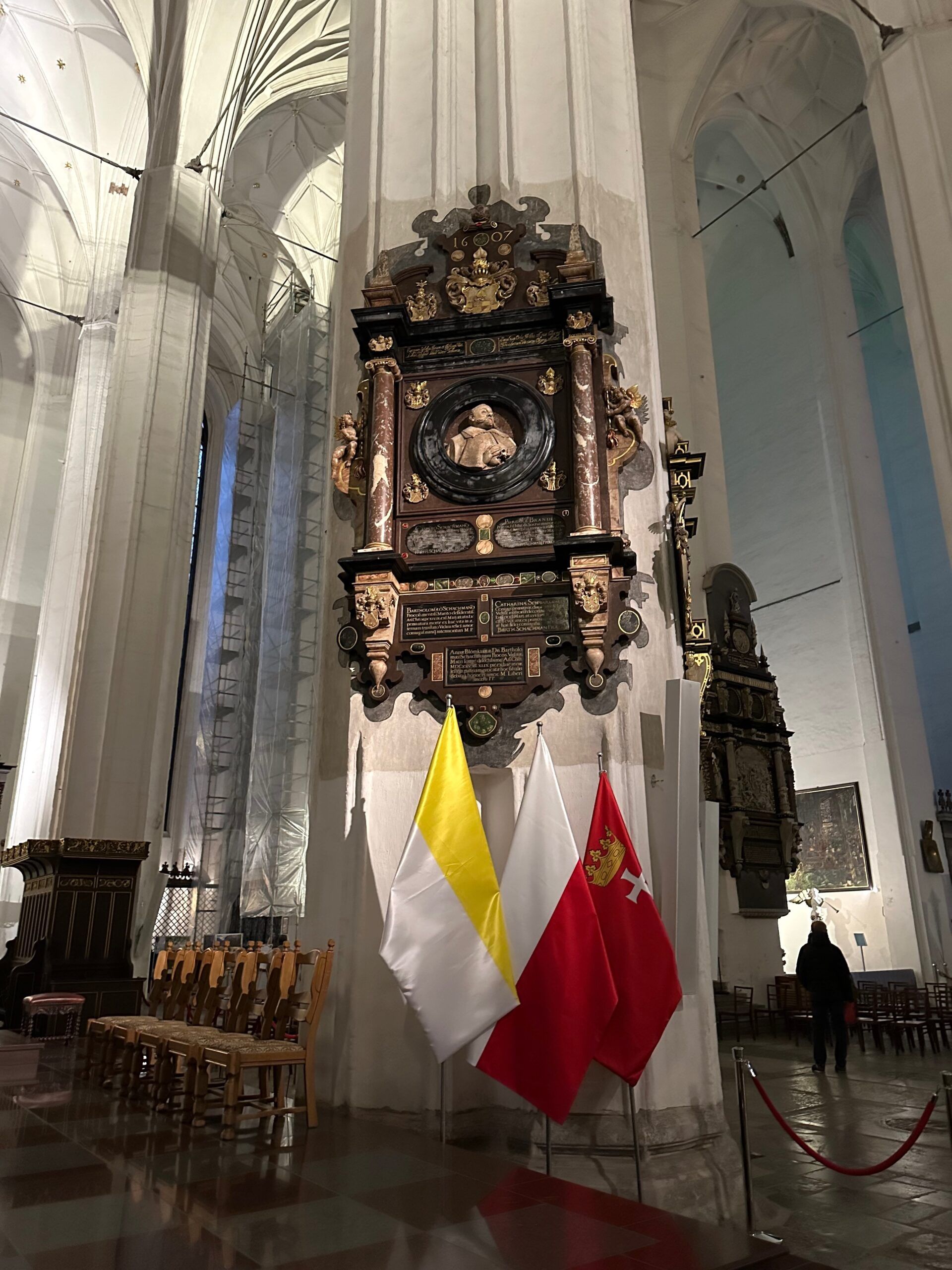 Wnętrze bazyliki mariackiej w gdańsku z ozdobnym zabytkowym ołtarzem i flagami.