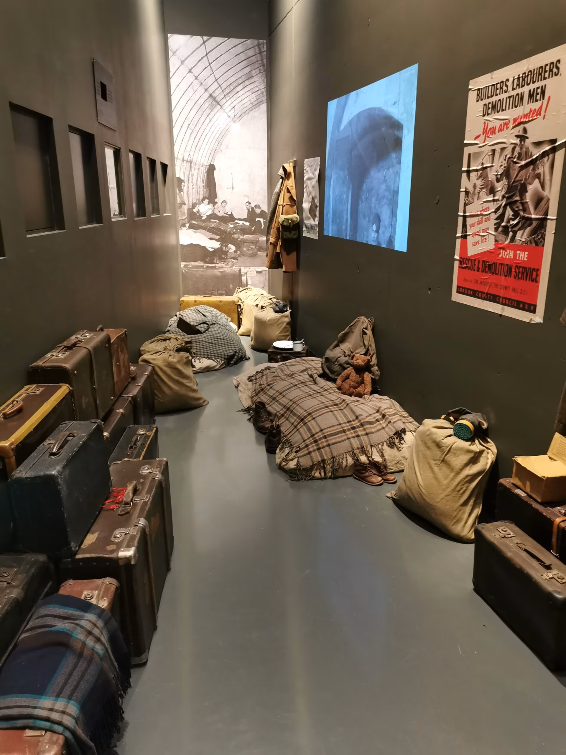 Ekspozycja w muzeum ii wojny światowej w gdańsku z pryczą, walizkami i plakatami wojennymi.