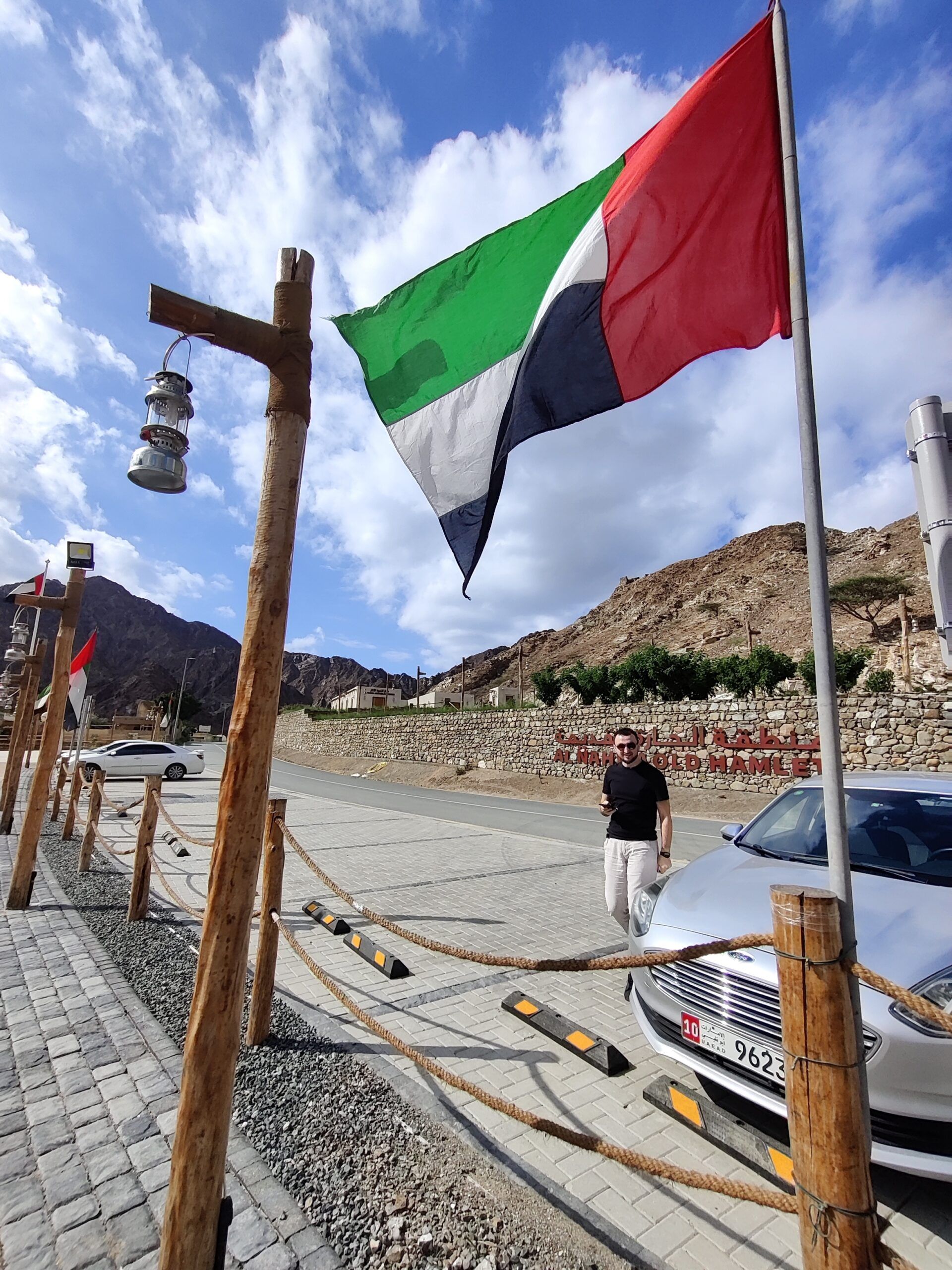 Flaga zjednoczonych emiratów arabskich przy nahwa w górach, obok drogi i zaparkowanego auta