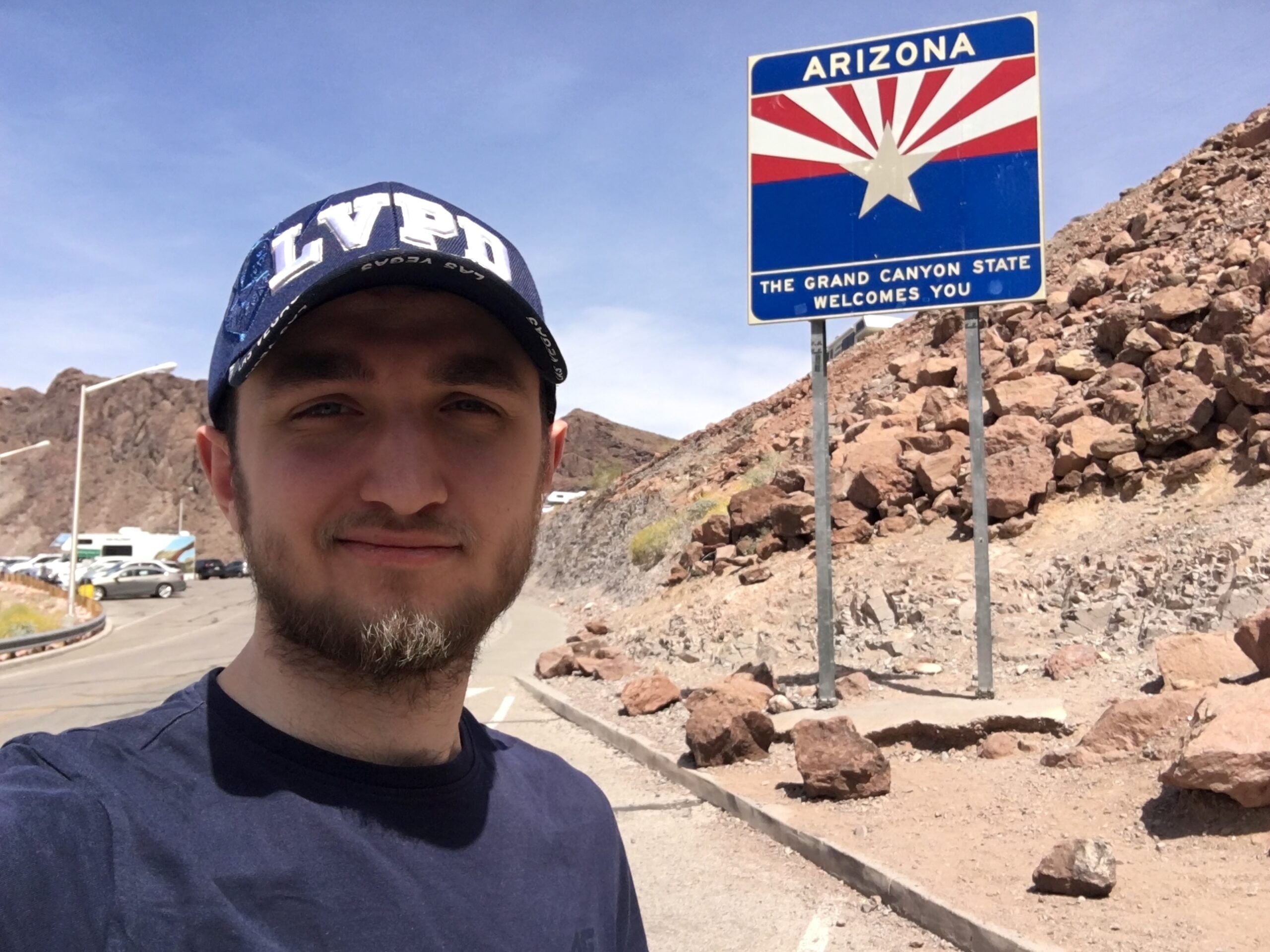 Mężczyzna robi selfie przy znaku arizona w pustynnym krajobrazie.