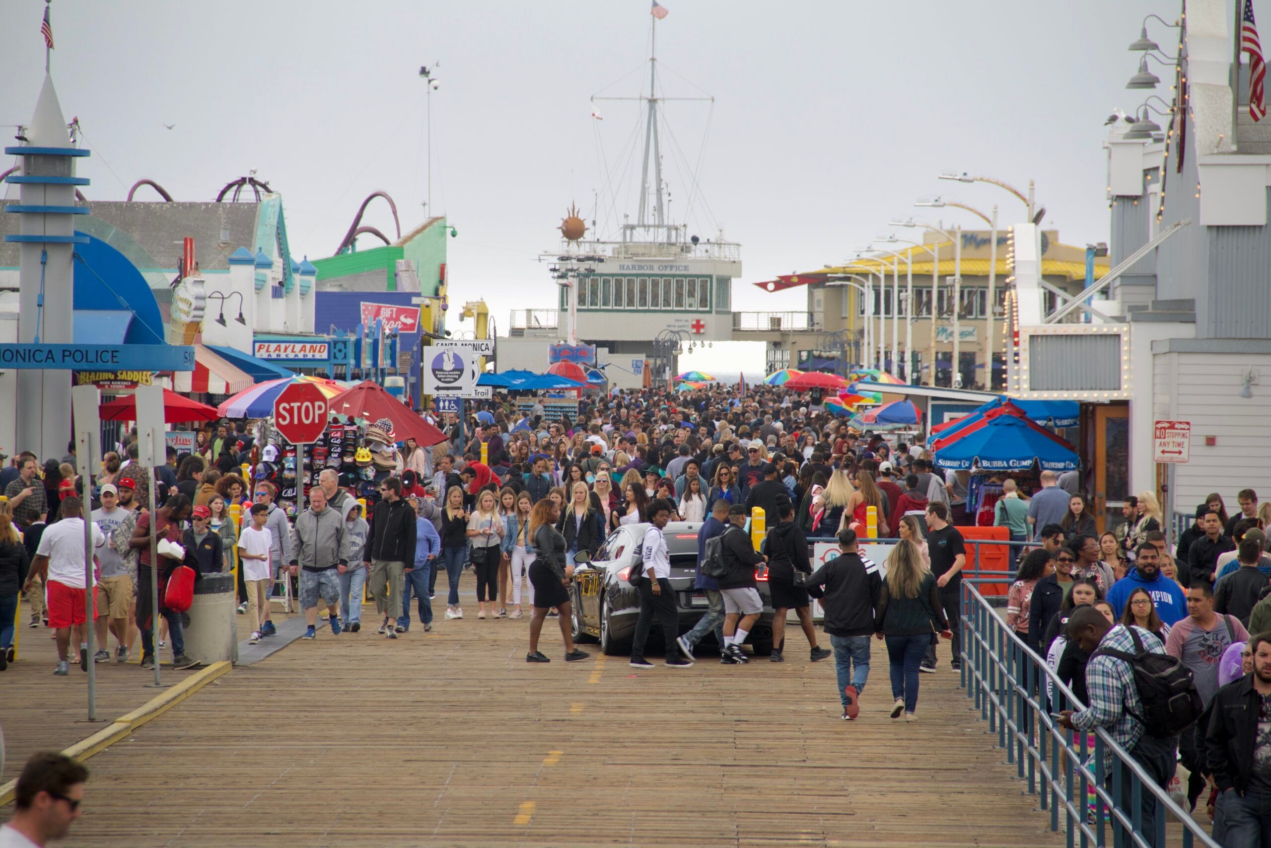 Tłum ludzi na molo w santa monica w los angeles, z kolorowymi budkami i parasolami.