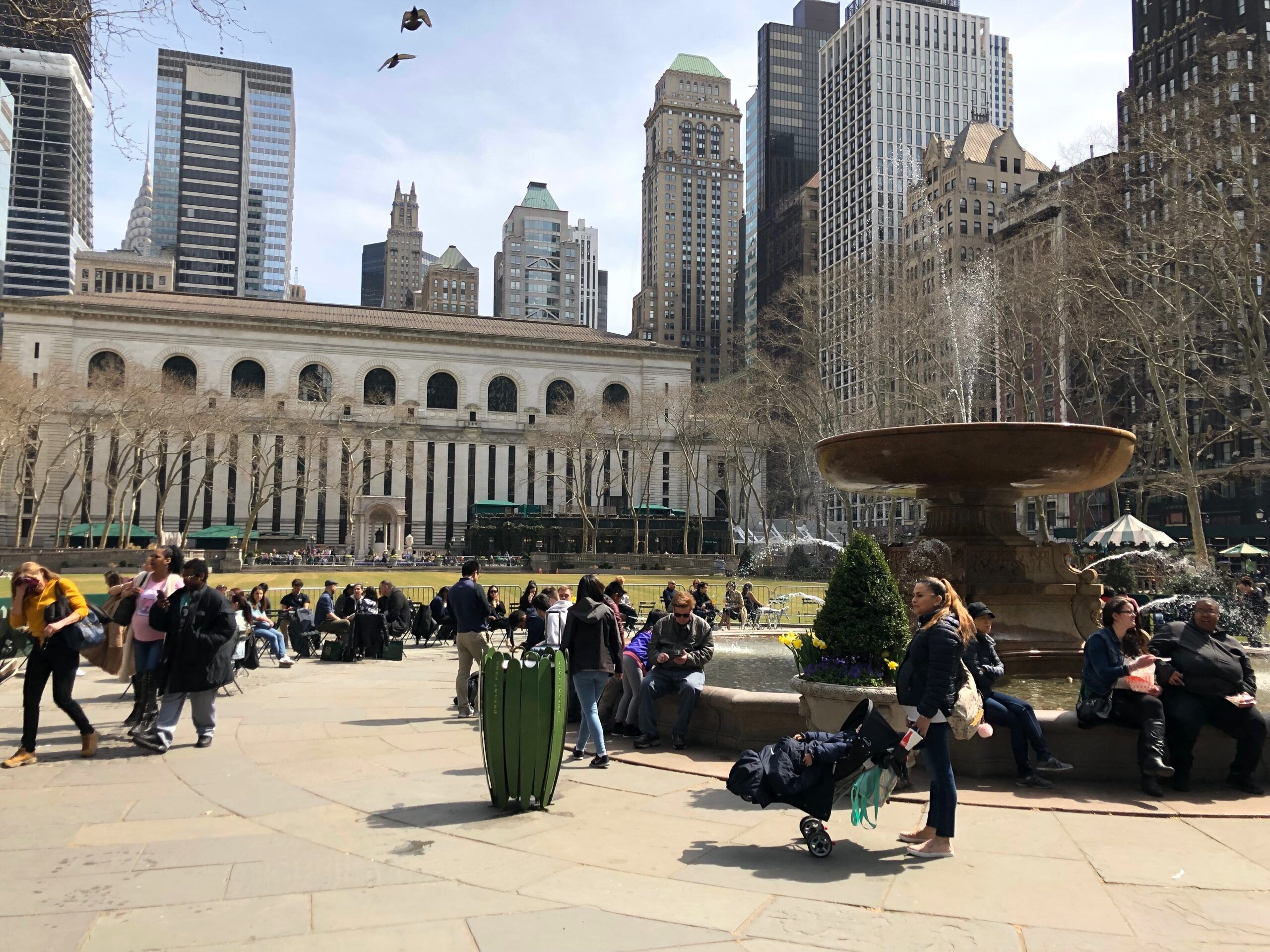 Bryant park w nowym jorku z fontanną, spacerującymi ludźmi i wieżowcami w tle