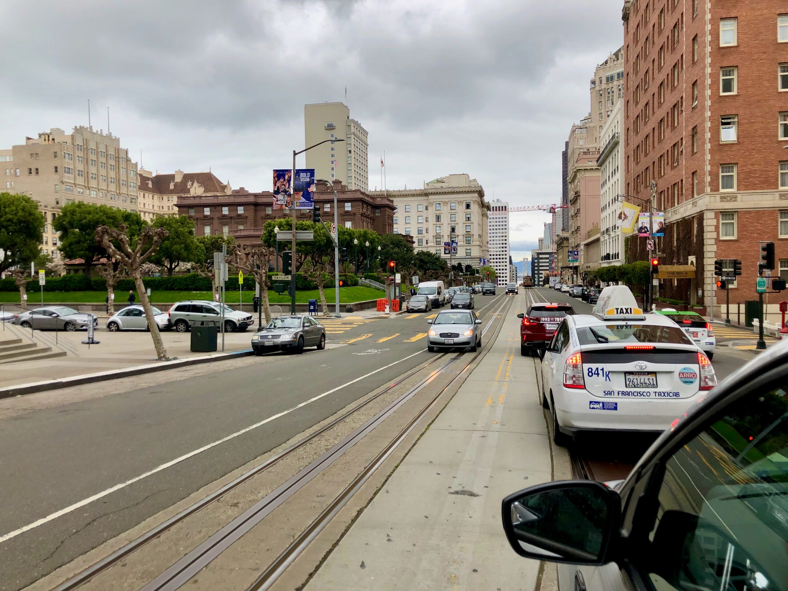 Ulica w san francisco z torowiskiem tramwajowym, taksówkami i miejską zabudową pod pochmurnym niebem