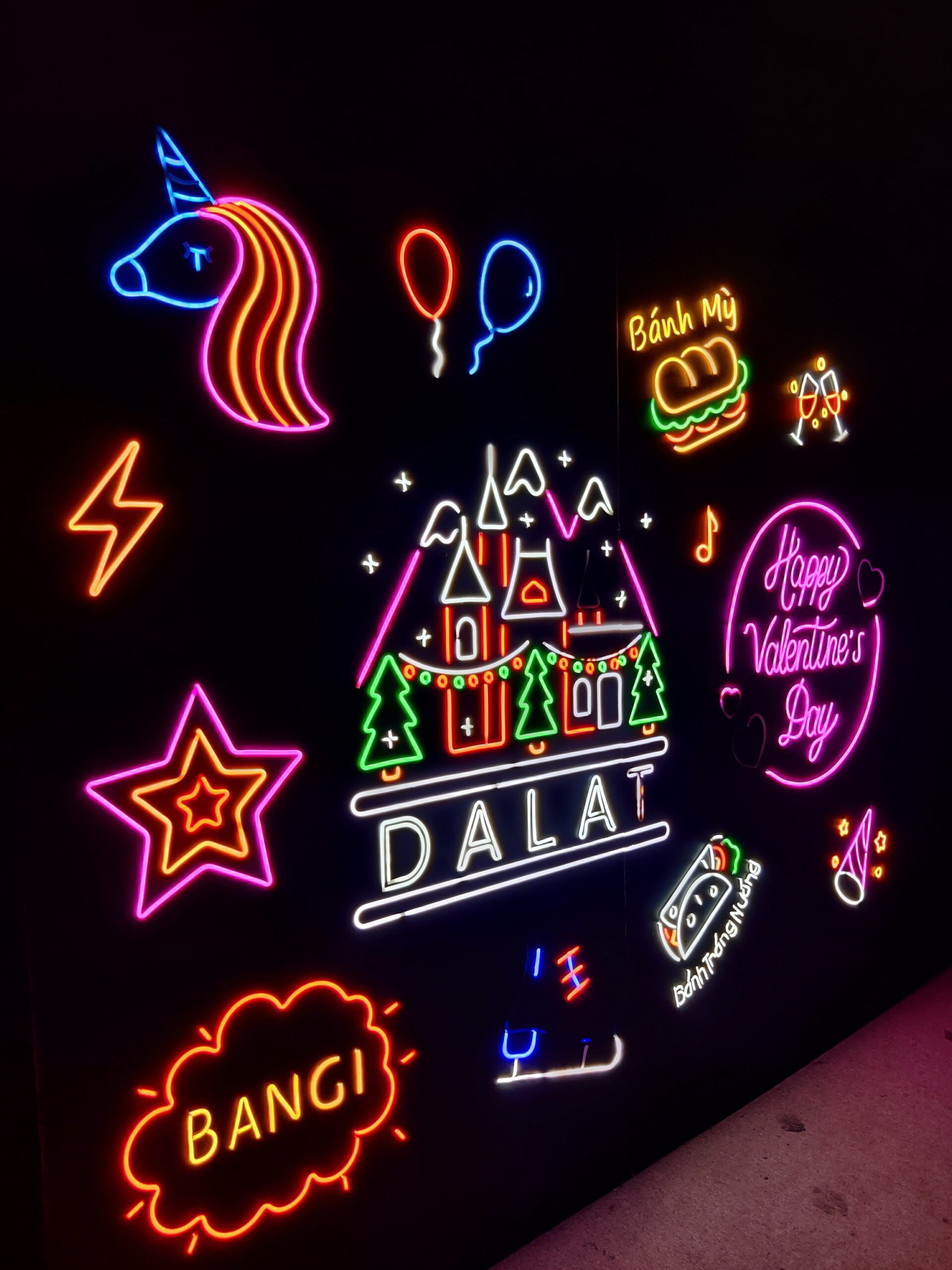 Neonowa ściana z napisami i ikonami w da lat light garden, w tym jednorożcem i dạlat.