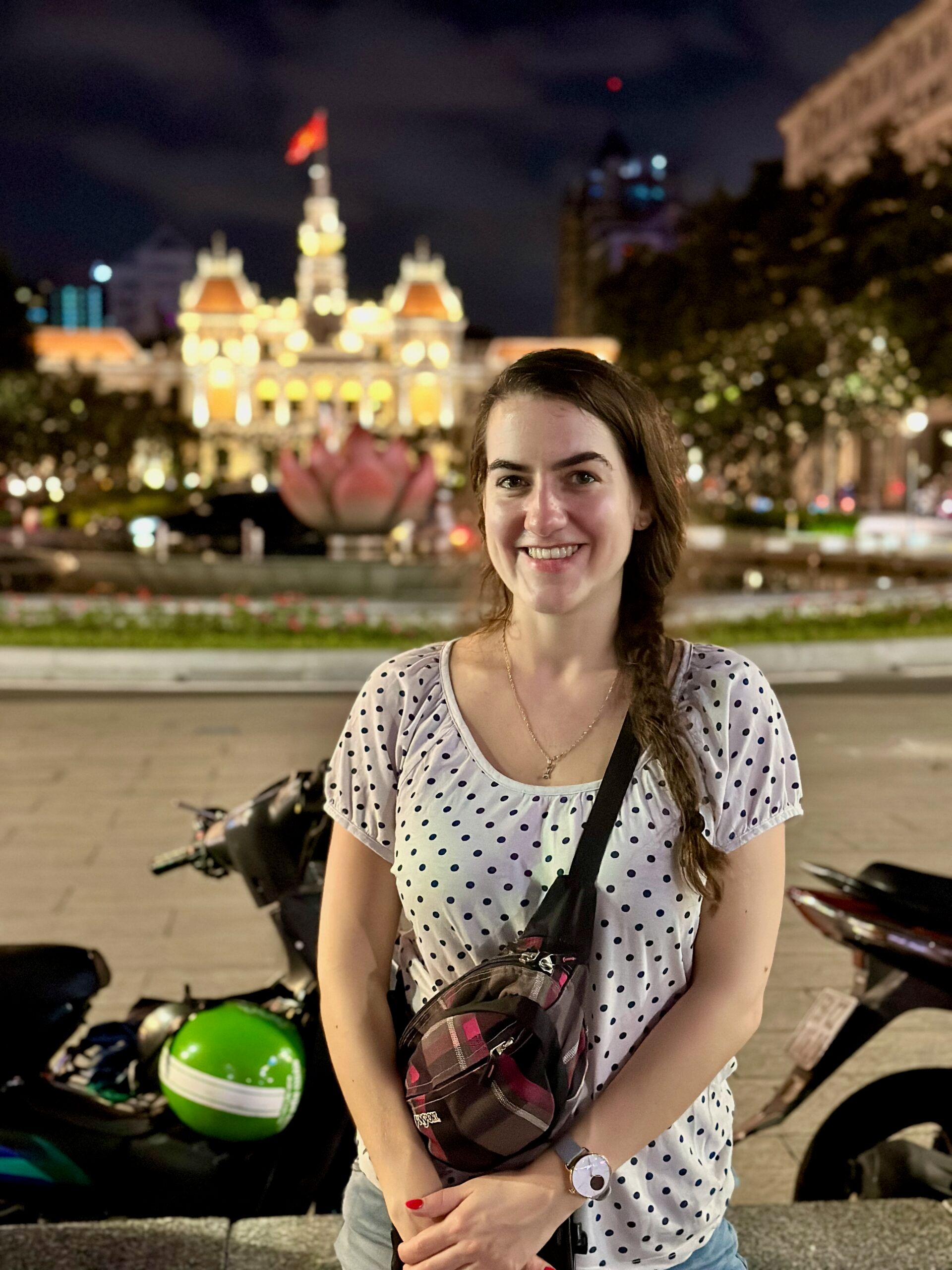Kobieta uśmiecha się na placu w ho chi minh, nocą, z podświetlonym zabytkowym budynkiem w tle.