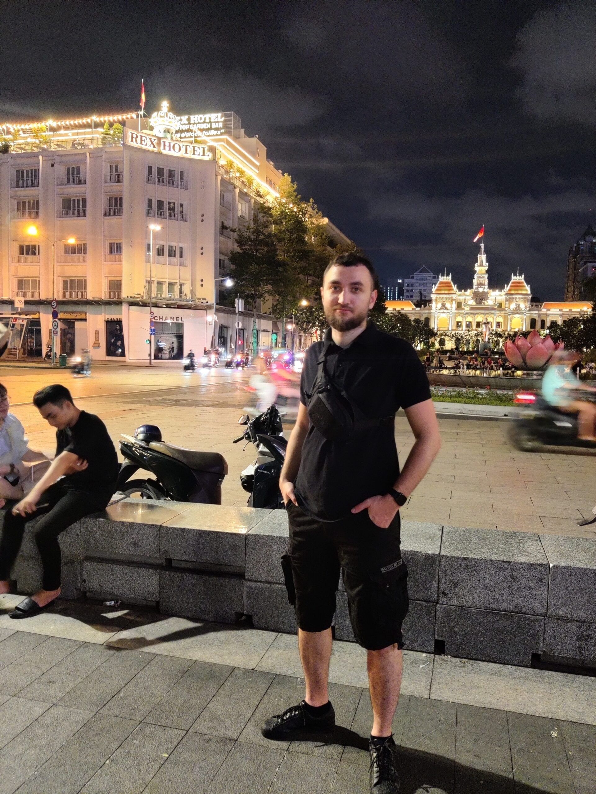 Ho chi minh square nocą, z mężczyzną stojącym na pierwszym planie i oświetlonym rex hotel w tle