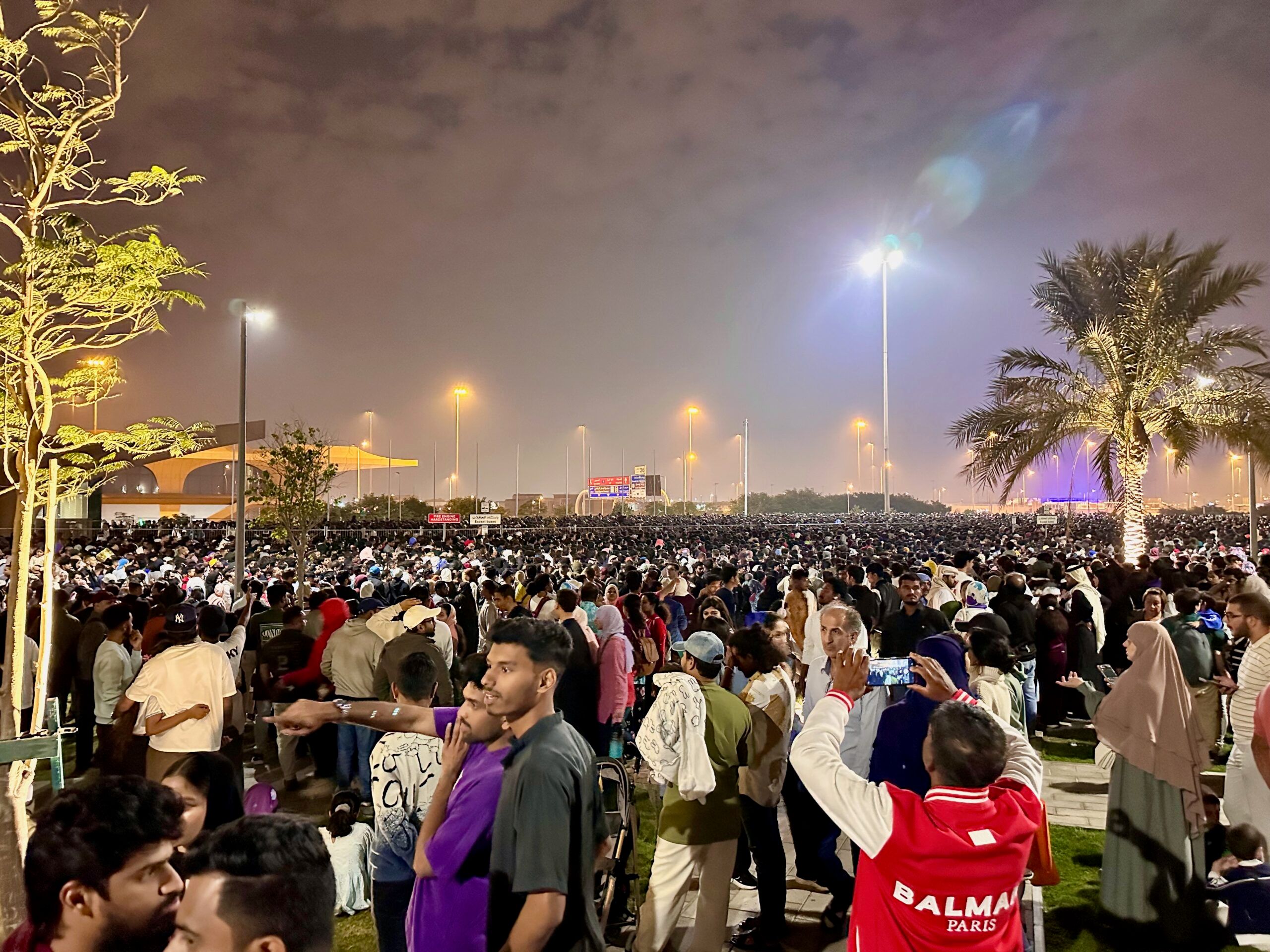 Tłum ludzi nocą w doha, pod ulicznymi latarniami i palmami