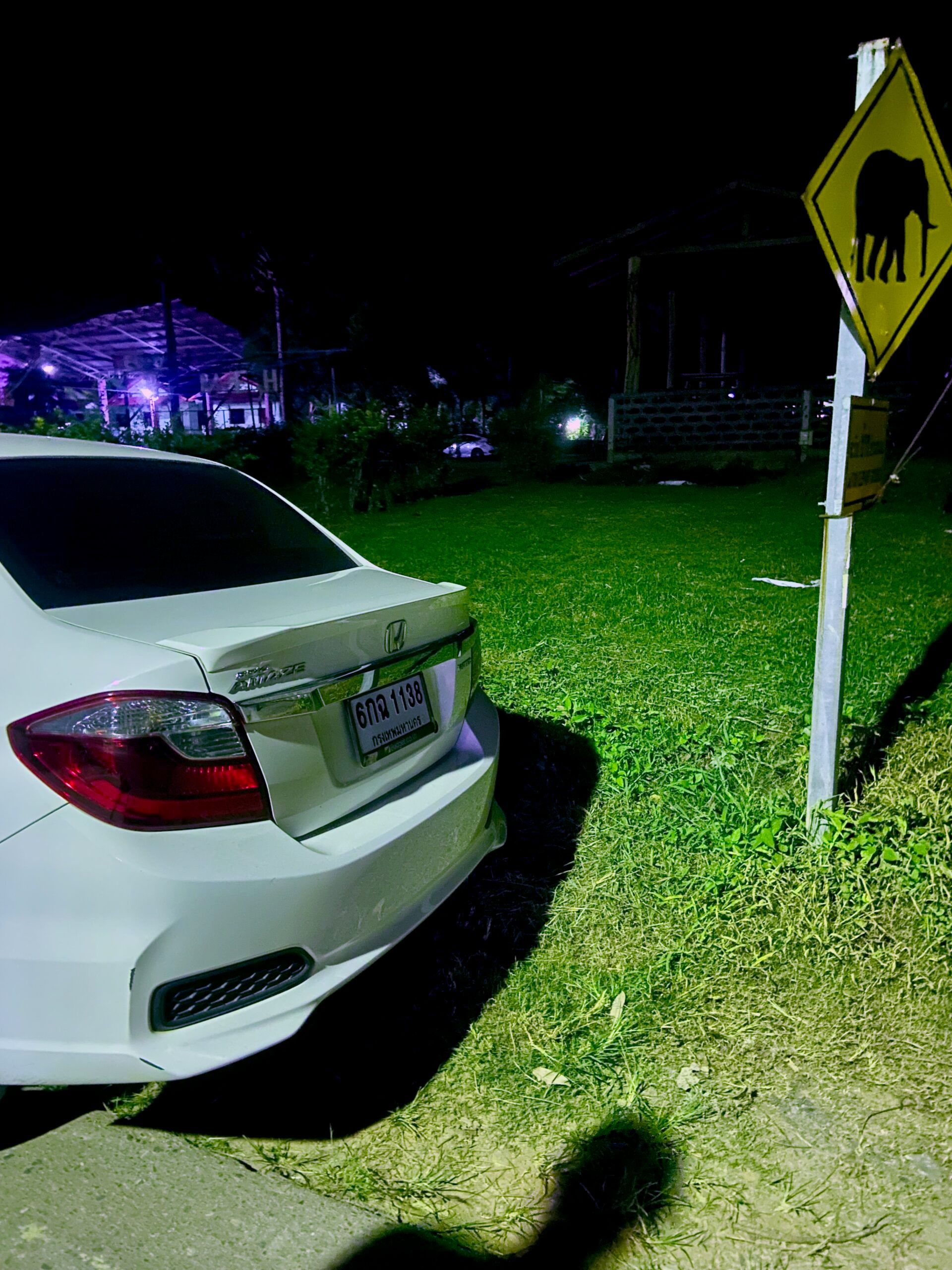 White car parked on the grass at night in koh chang, thailand, next to a yellow sign.
