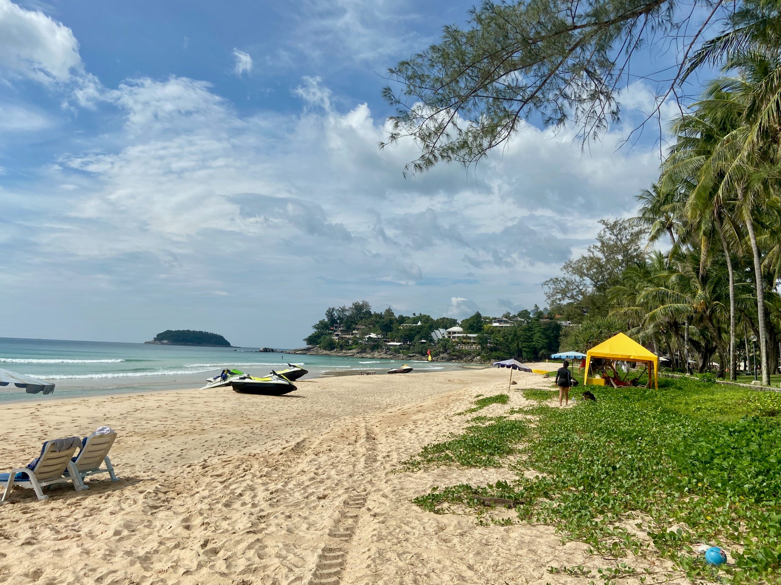 Plaża na phuket w tajlandii z palmami, leżakami i skuterami wodnymi przy brzegu.