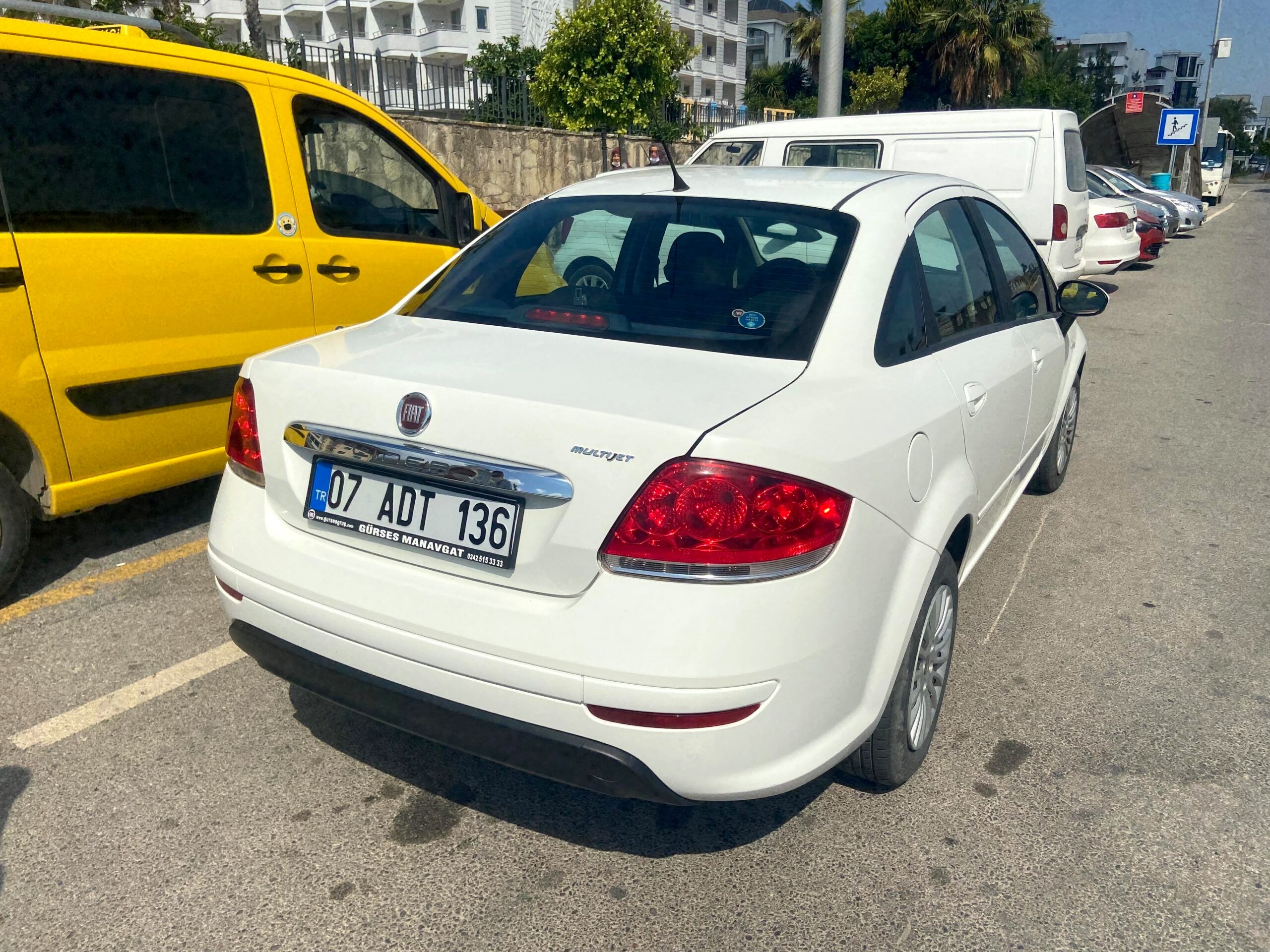 Biały fiat grande punto na parkingu w antalyi, obok żółtego vana.