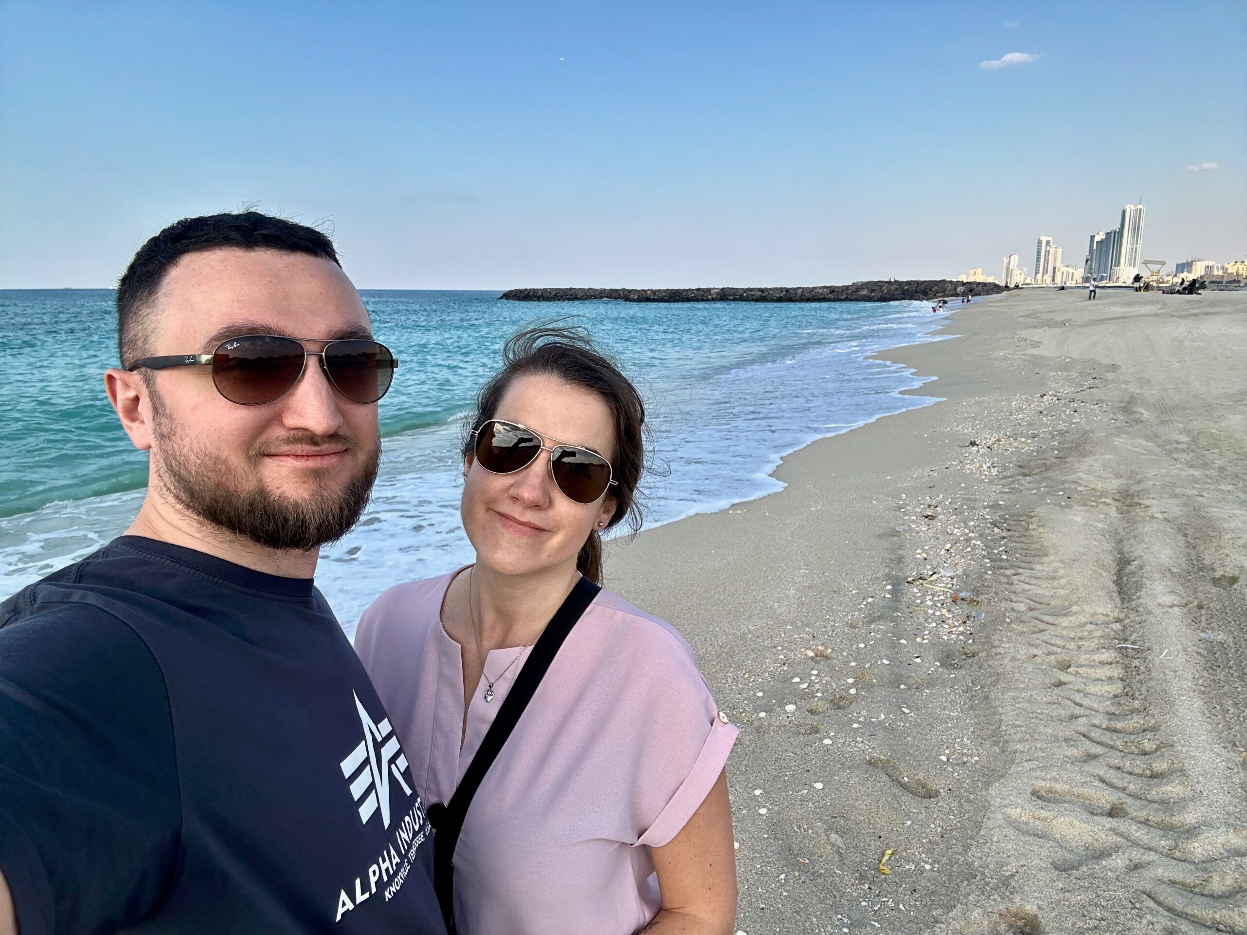 Para na plaży heera beach w sharjah, z morzem i panoramą wieżowców w tle