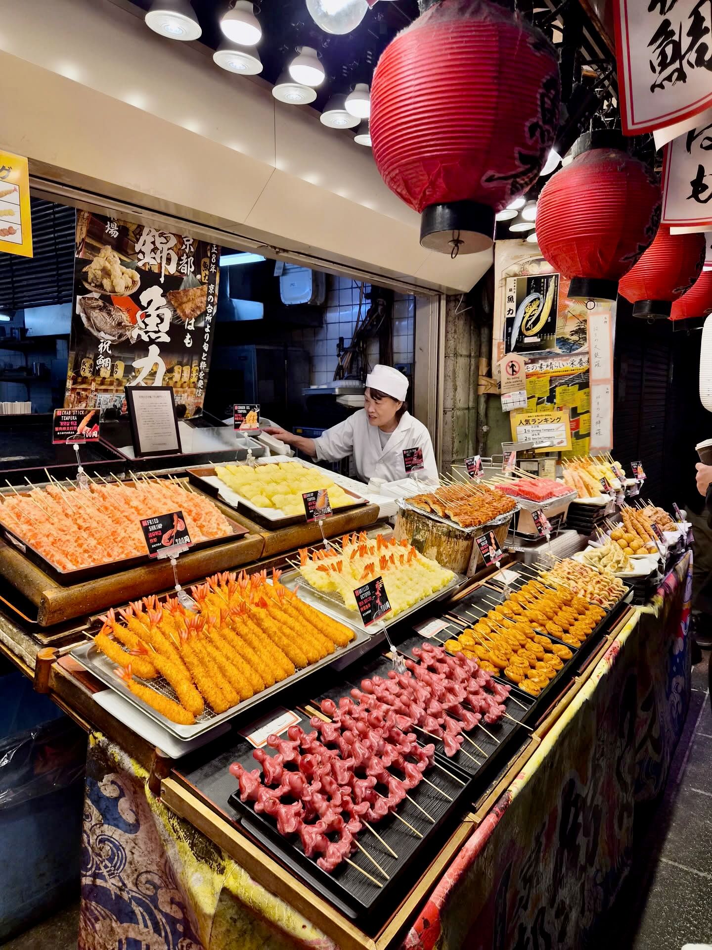Stoisko z przekąskami w nishiki market w kioto, z różnymi smażonymi szaszłykami i pracownicą za ladą