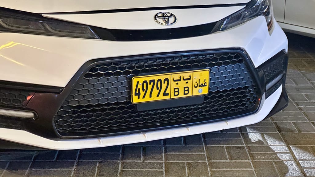 Przód białego samochodu toyota z żółtą tablicą rejestracyjną w muscacie, oman.