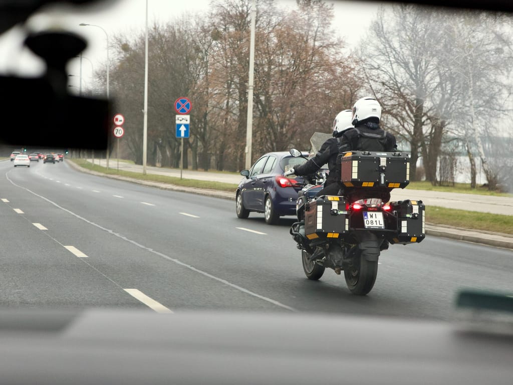 Dwóch motocyklistów jedzie ulicą w warszawie, z kuframi i białymi kaskami.
