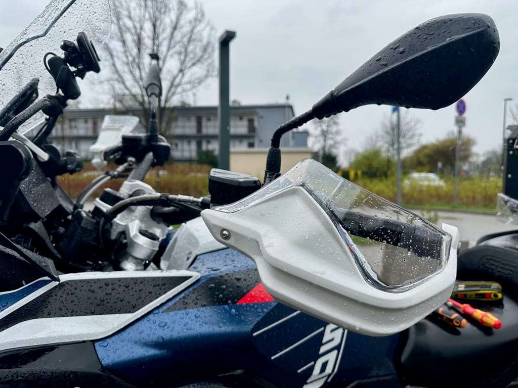 Zbliżenie na bmw r1250gs z mokrym lusterkiem i osłoną dłoni po deszczu.