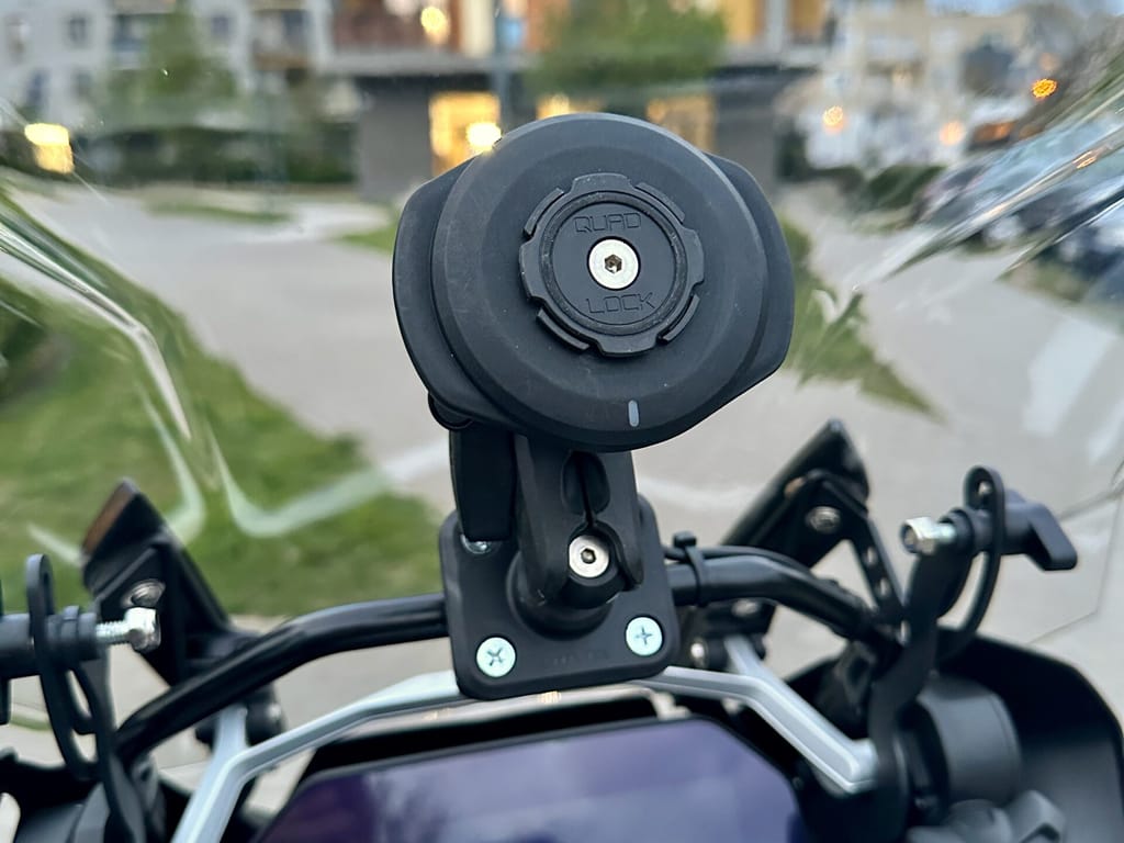 Kokpit motocykla bmw r1250gs z uchwytem na telefon na tle osiedlowych budynków.