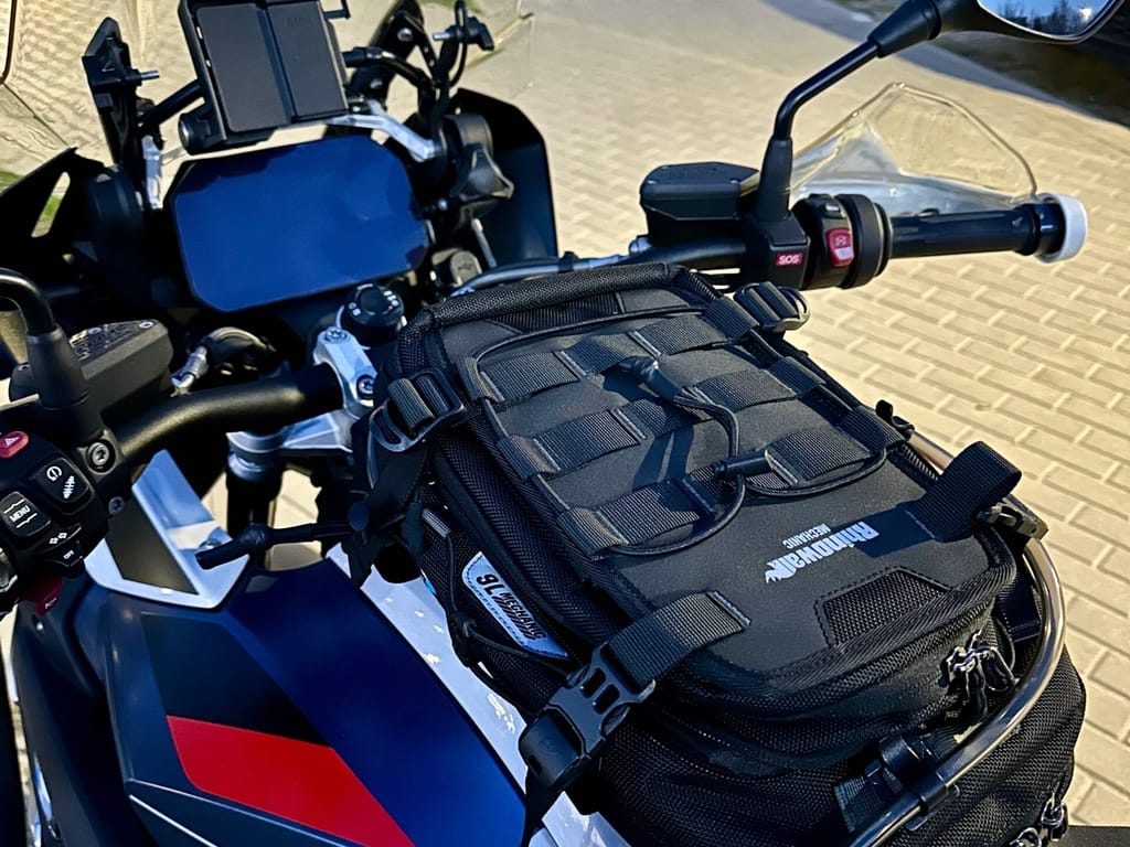 Motocykl bmw r1250gs z torbą na baku, widok kokpitu i kierownicy przy chodniku.