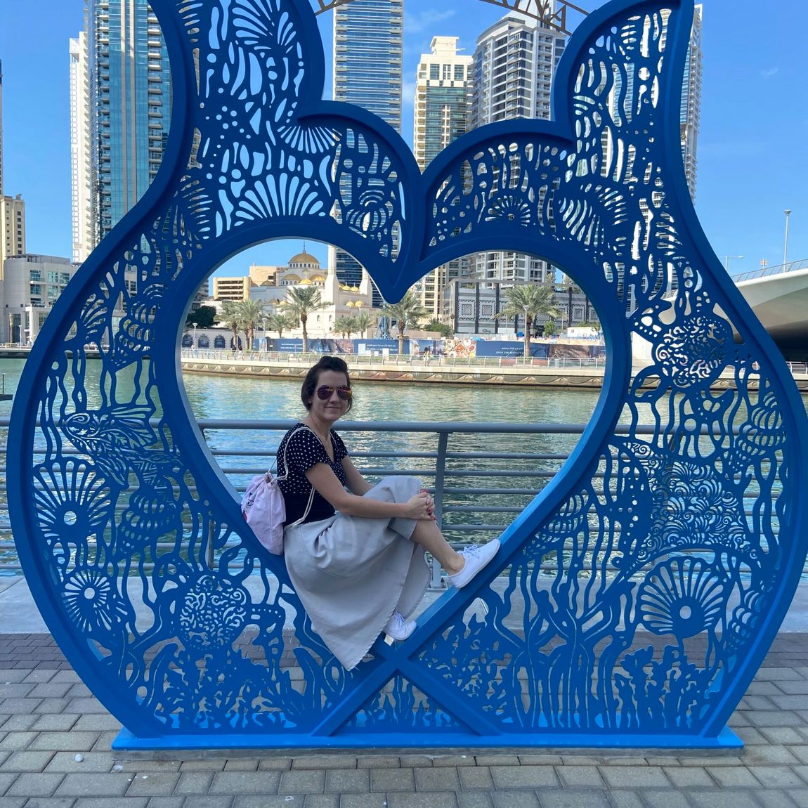 Osoba siedzi w niebieskiej ramie z napisem dubai marina nad wodą i wieżowcami w tle.