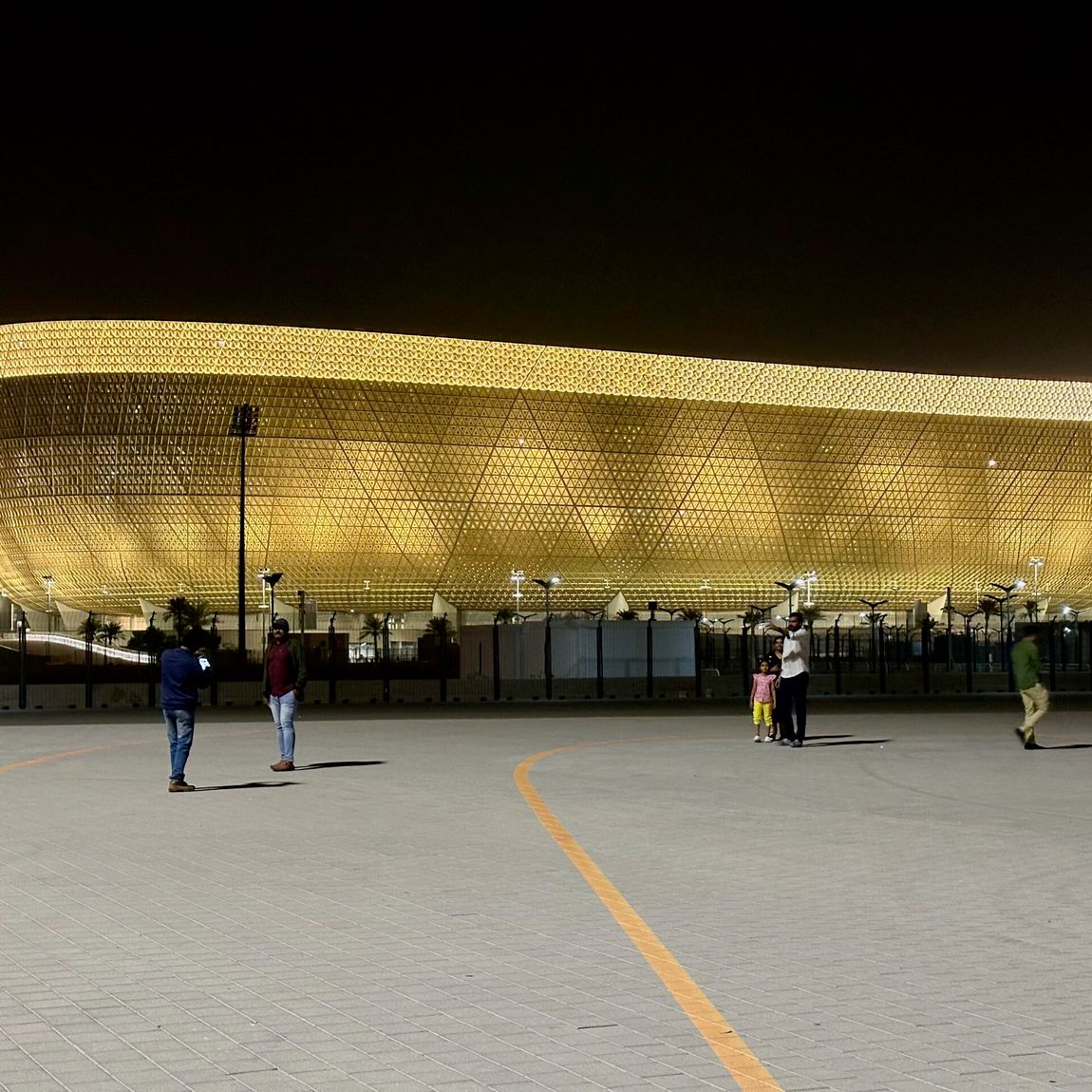 Złocisty stadion w doha nocą, z kilkoma ludźmi na placu przed nim