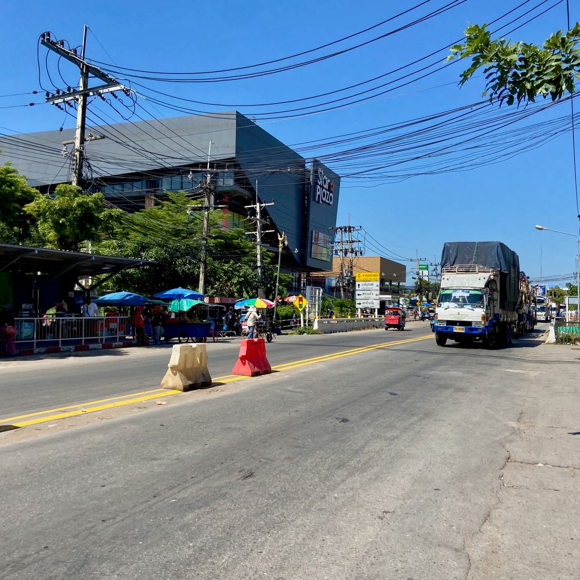 Street view in ubon ratchathani, thailand, with trucks, power lines, and colorful bags on the roadside