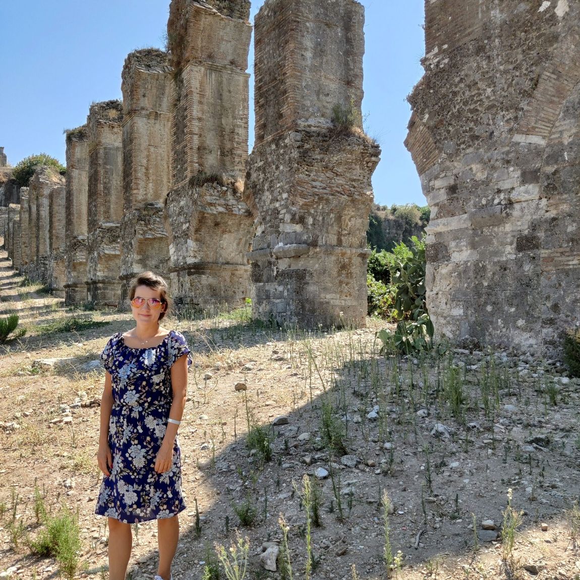 Aspendos aqueduct w turcji, z kobietą stojącą przy kamiennych arkadach.
