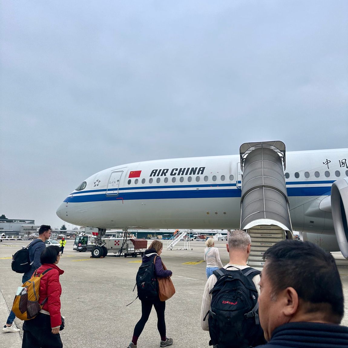 Pasażerowie idą po płycie lotniska do samolotu air china w mediolanie.