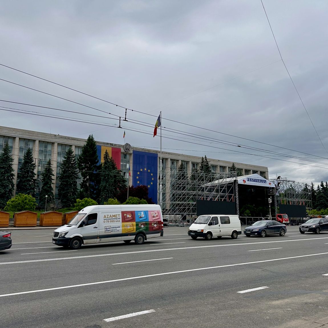 Chisinau road conditions in moldova with vehicles parked near a building and festival stage setup under cloudy sky
