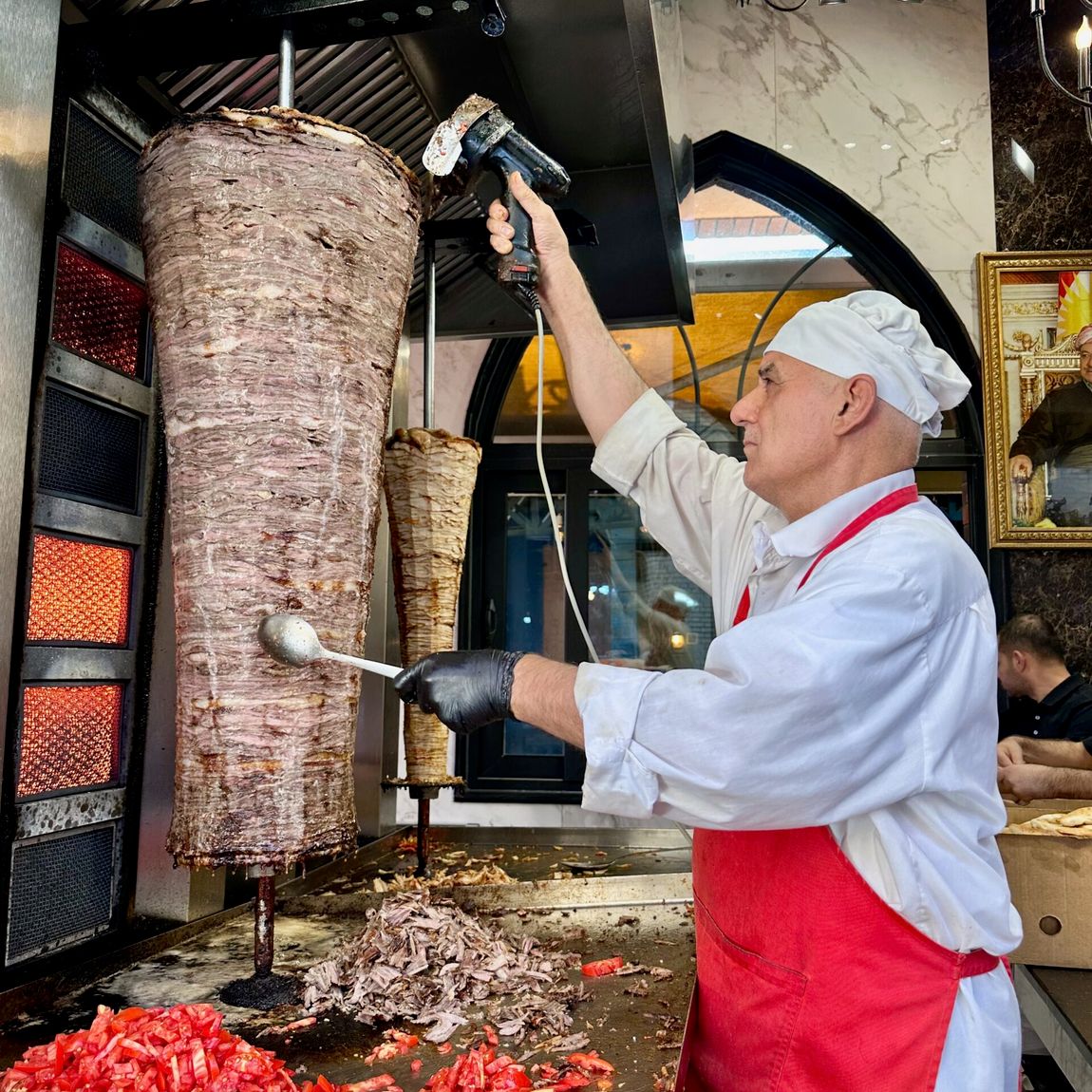 Kucharz przy pionowym rożnie z mięsem w erbil foods, obok pokrojone pomidory.